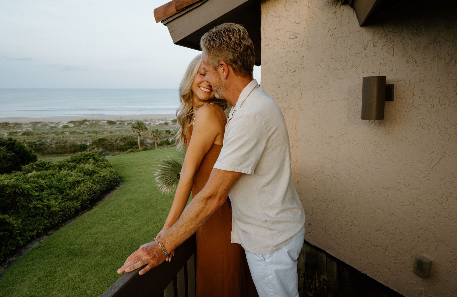 Couple sharing a romantic moment on a balcony overlooking a lush beachside landscape at the Omni Resort on Amelia Island, Florida.