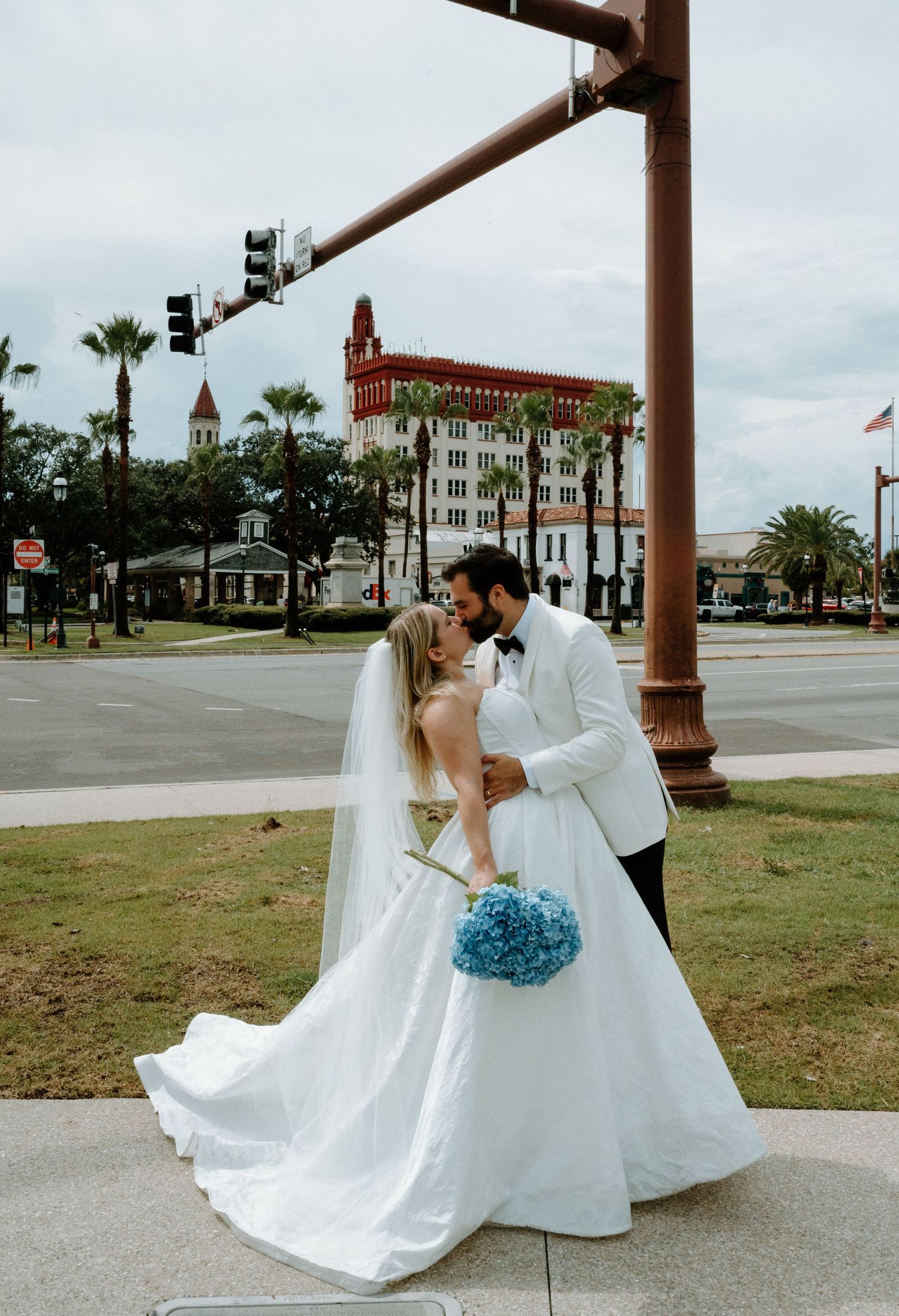 Wedding couple sharing a kiss outdoors with blue hydrangea bouquet and historic building backdrop in Saint Augustine, Florida.