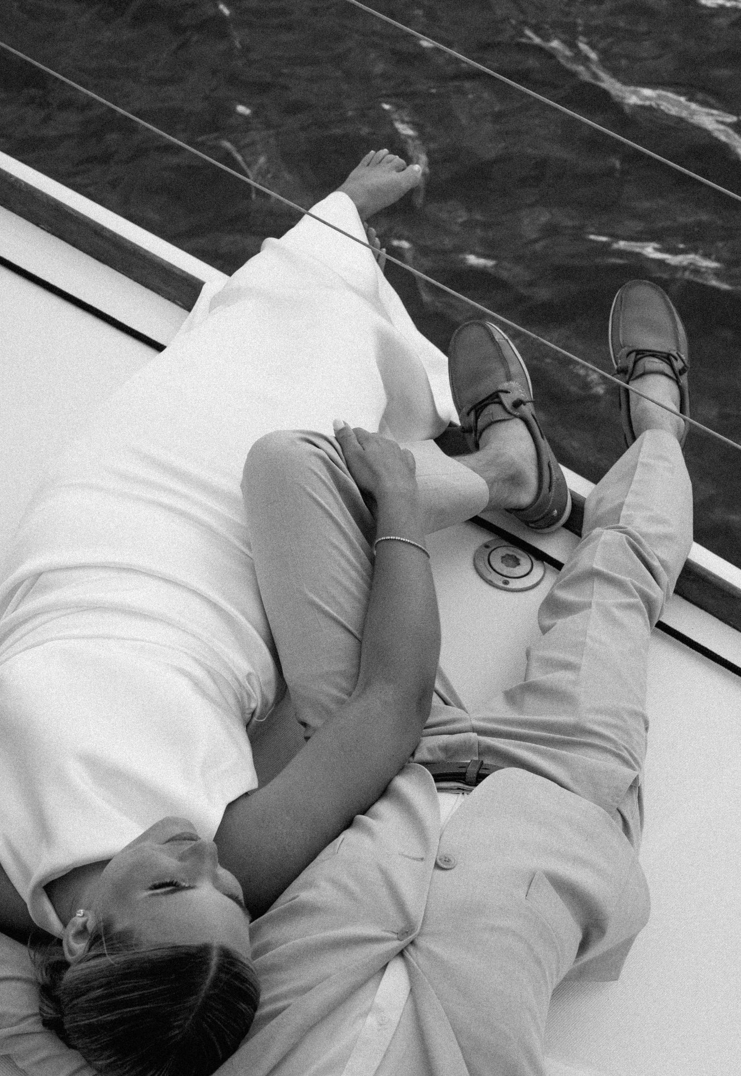 Black and white overhead photo of bride and groom lying together on a sailboat deck.