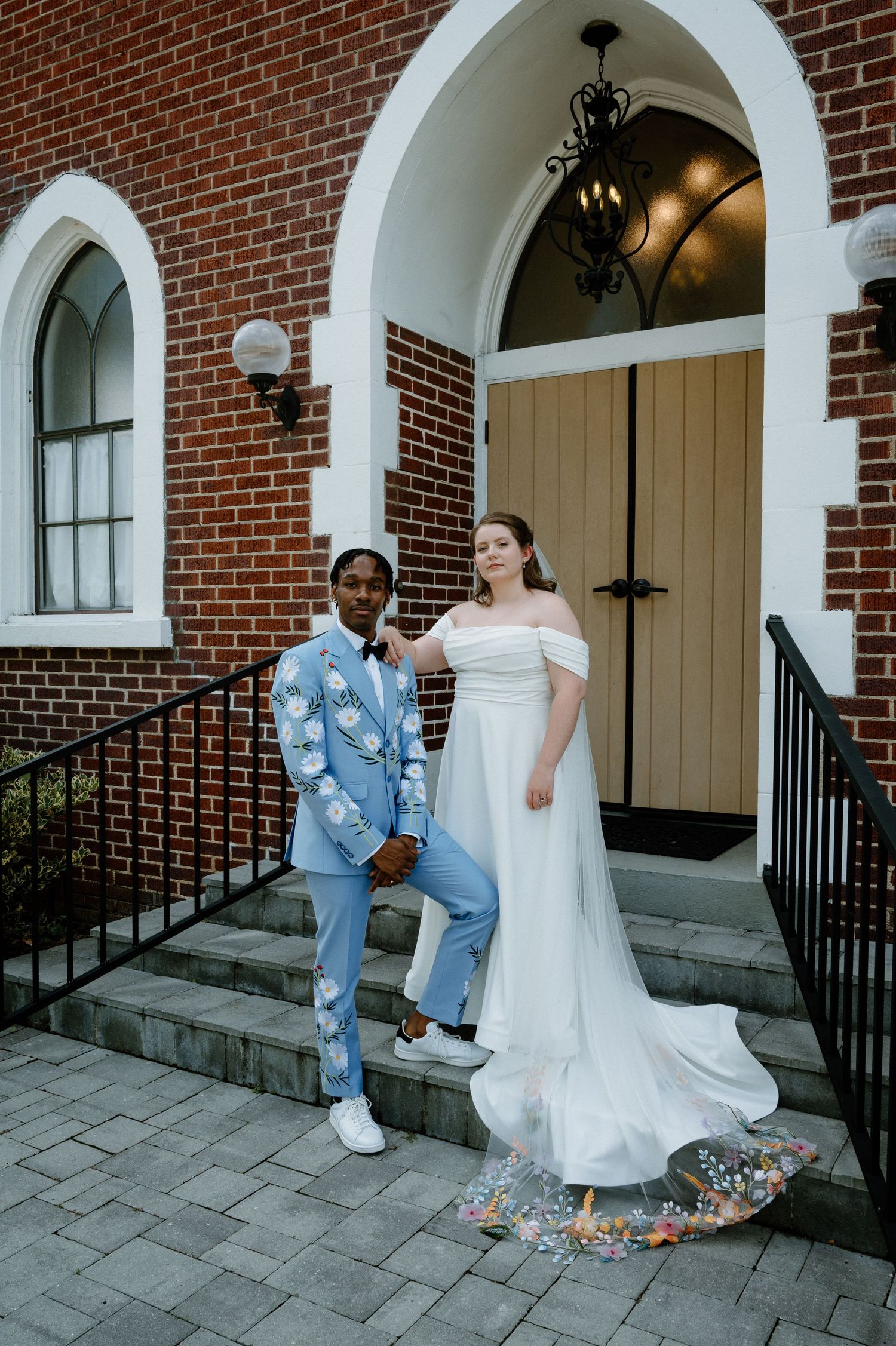 Groom in blue floral suit and bride in off-shoulder gown pose on brick church steps in Jacksonville, Florida.