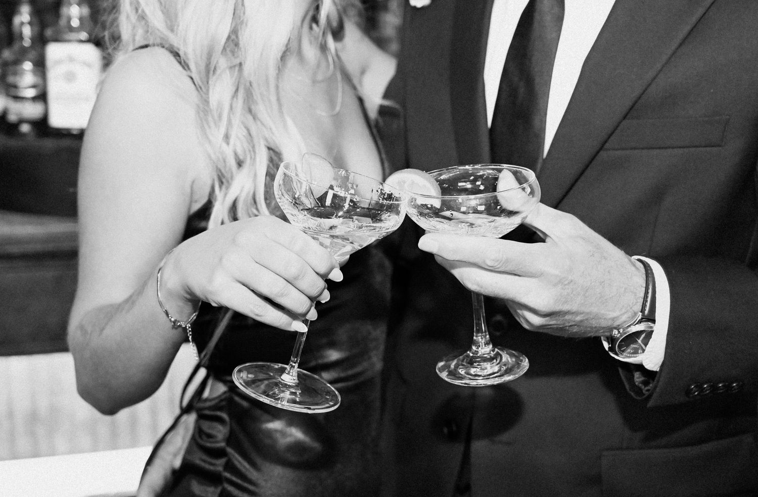 Black and white photo of couple clinking champagne glasses at elegant bar event.
