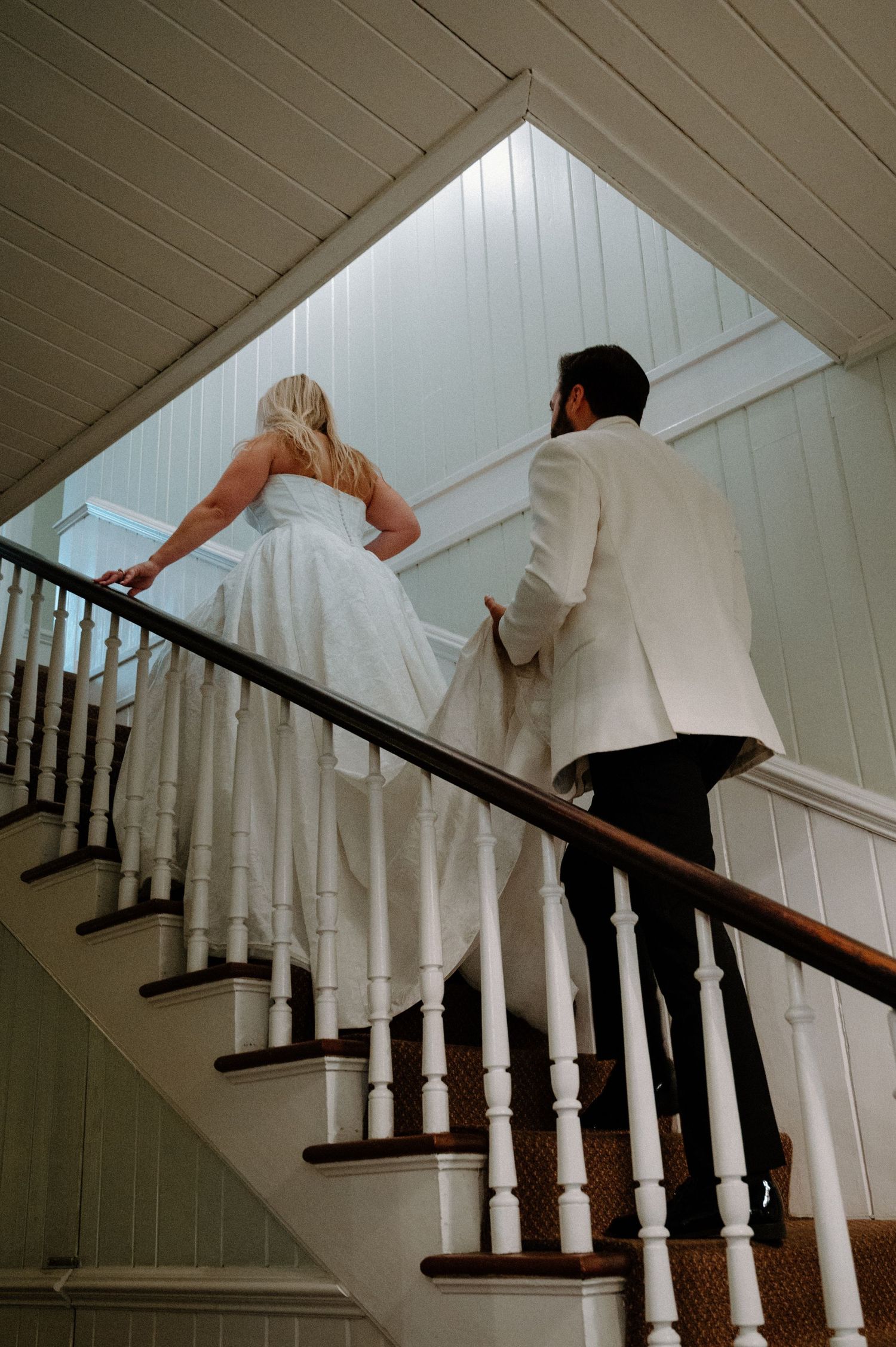 Bride and groom walking up elegant white staircase with wooden railing on their wedding day at the Kenwood Inn in Saint Augustine, Florida.