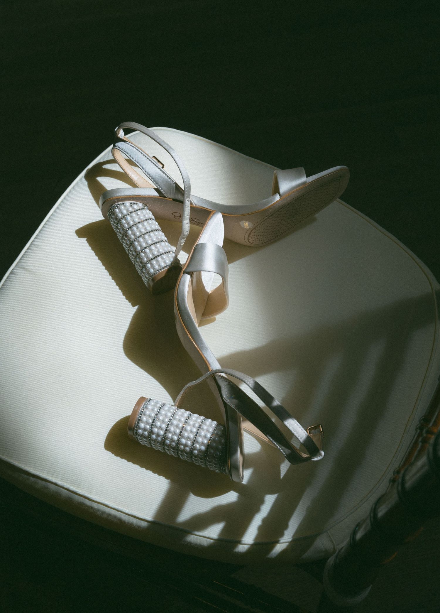 Silver strappy wedding heels with checkered block heels resting on a white surface in dramatic lighting.