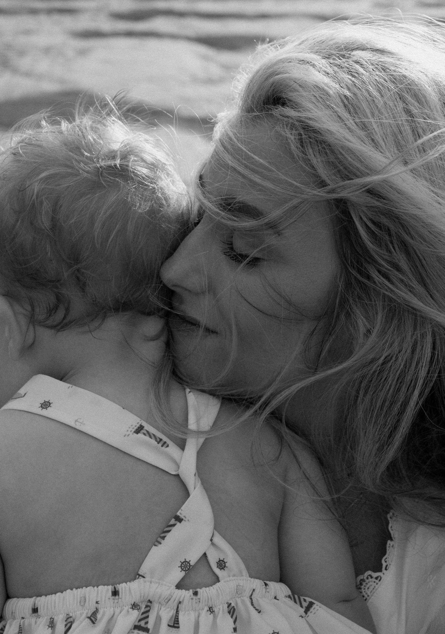 Black and white tender moment of a blonde mother gently kissing her young childs head.