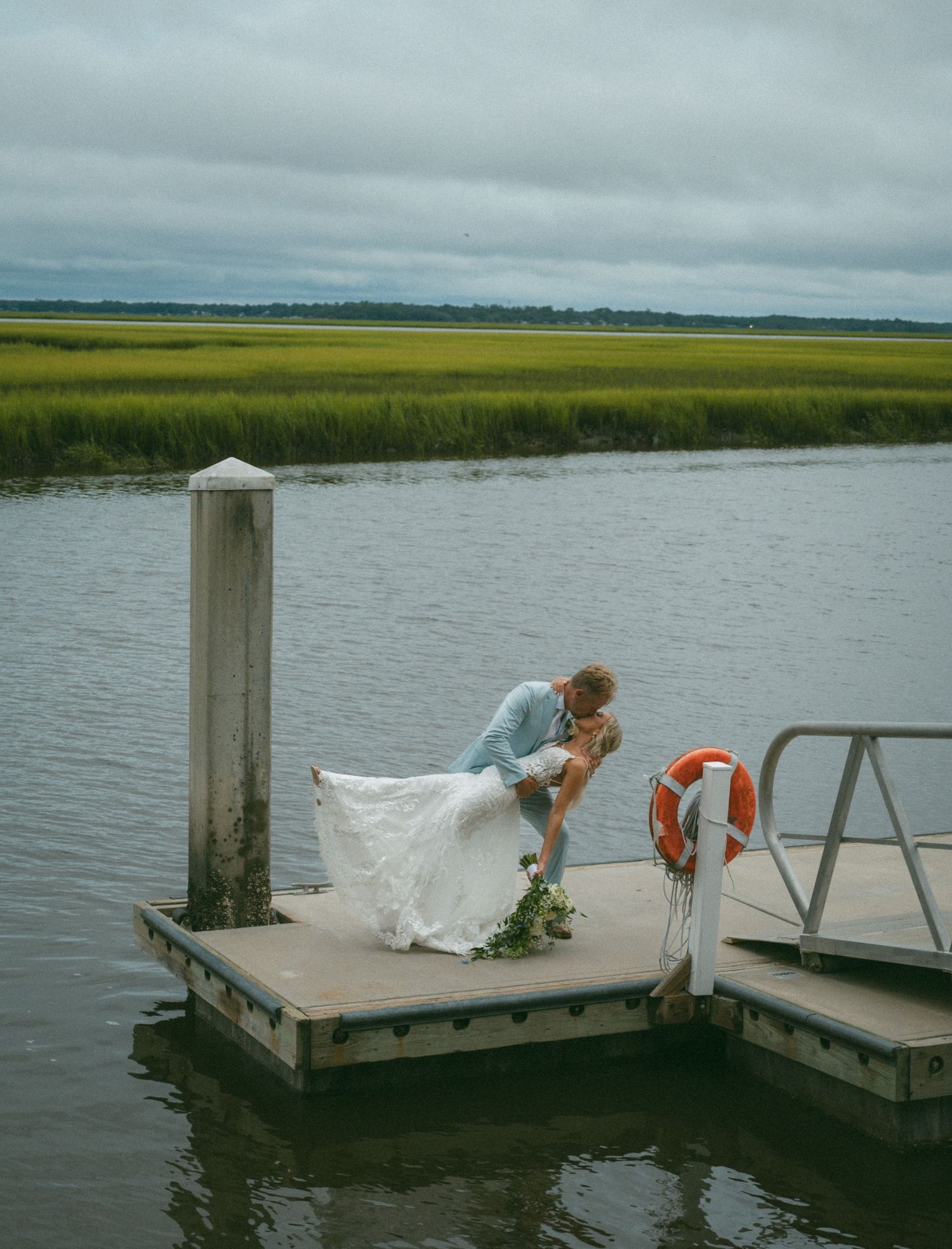 Groom dips bride in a romantic kiss on a floating dock surrounded by marsh and water at Walker's Landing on Amelia Island, Florida.