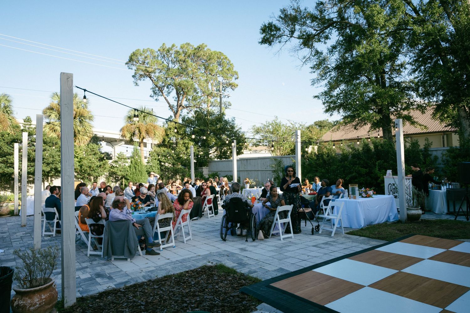 Outdoor wedding reception with guests seated on white chairs around a checkered dance floor at golden hour in Jacksonville, Florida.
