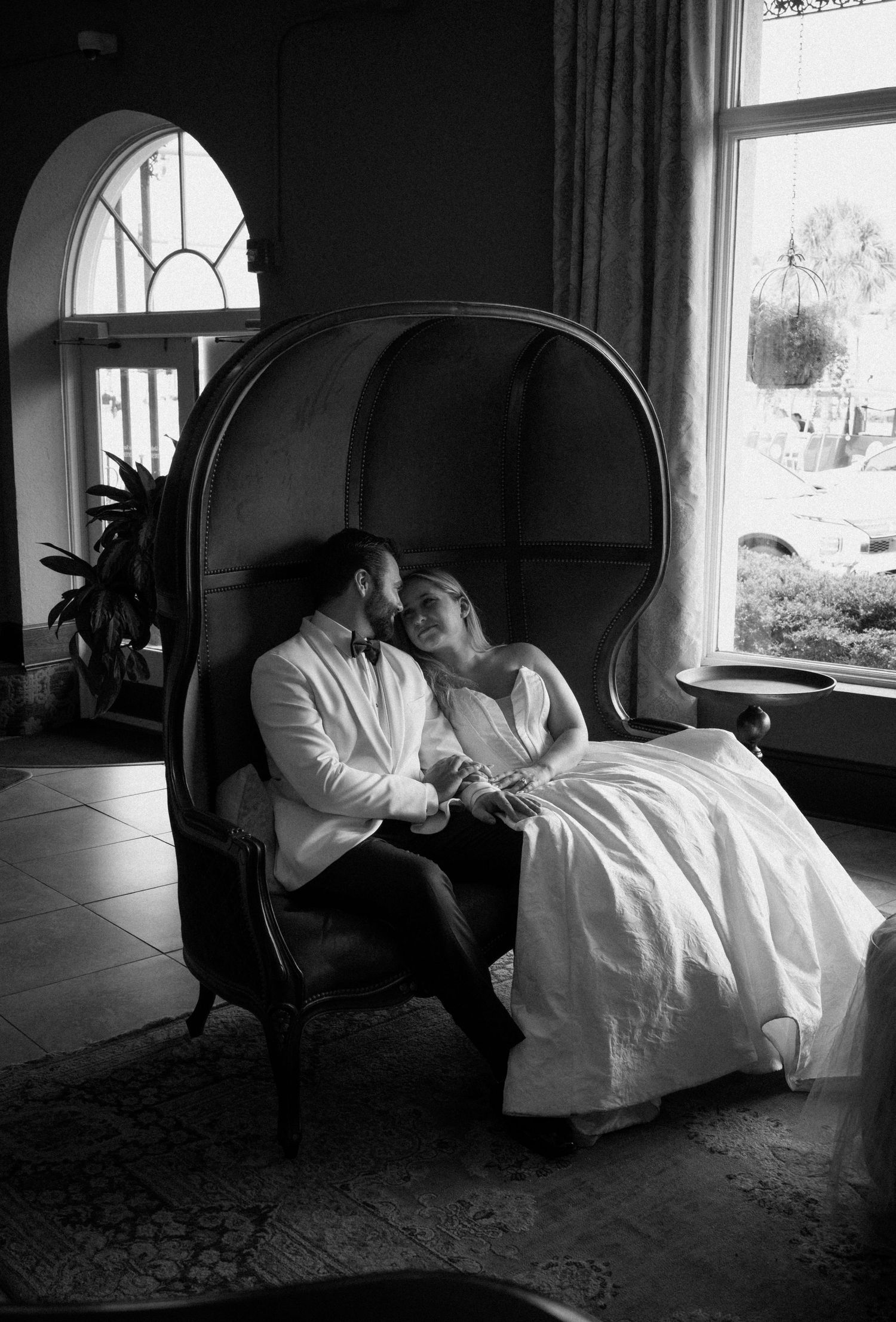 Bride and groom sharing an intimate moment seated in an elegant dome chair in black and white.