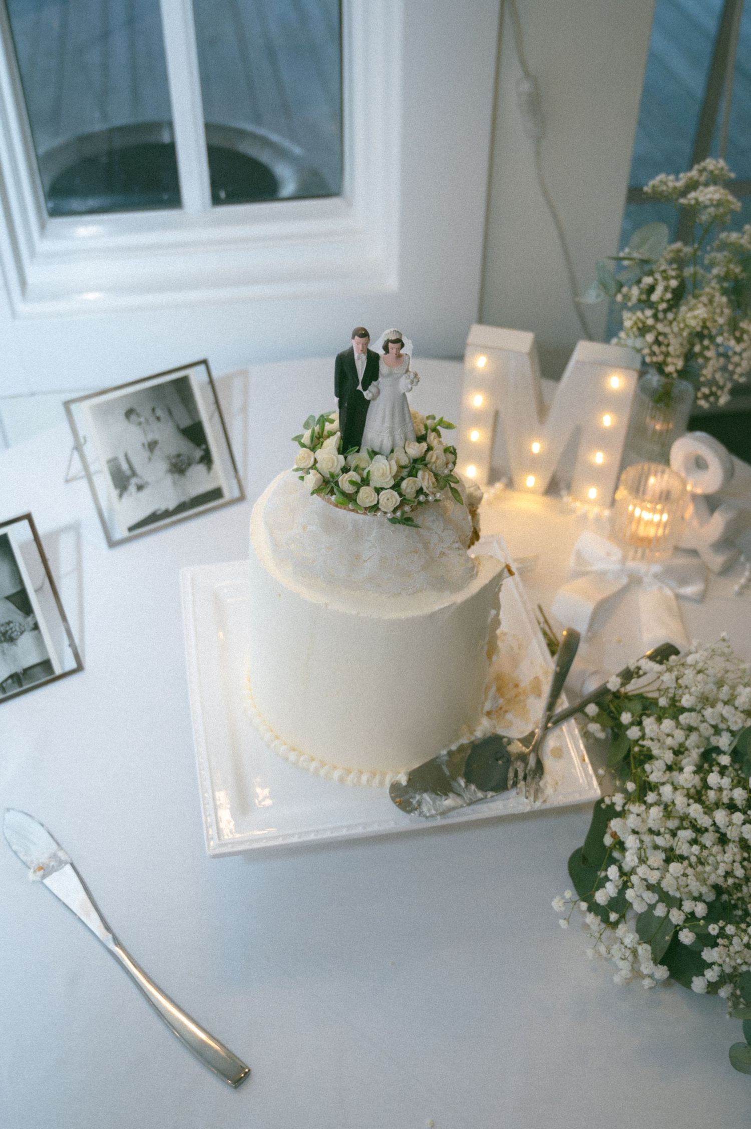 Elegant single-tier white wedding cake with bride and groom topper and floral decorations on display table.