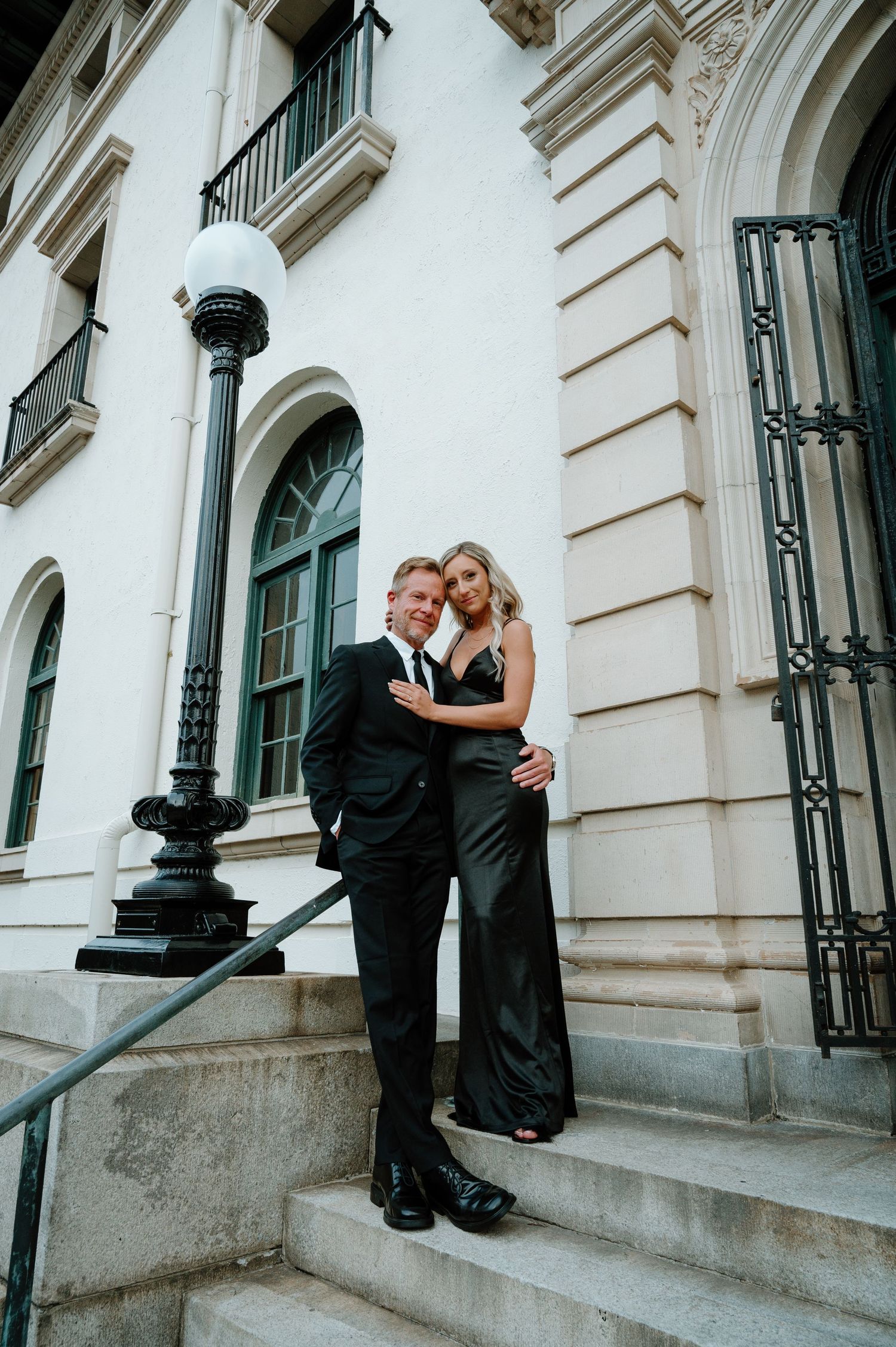 Stylish couple in matching black formal attire posing on steps of a the historic post office on Amelia Island, Florida