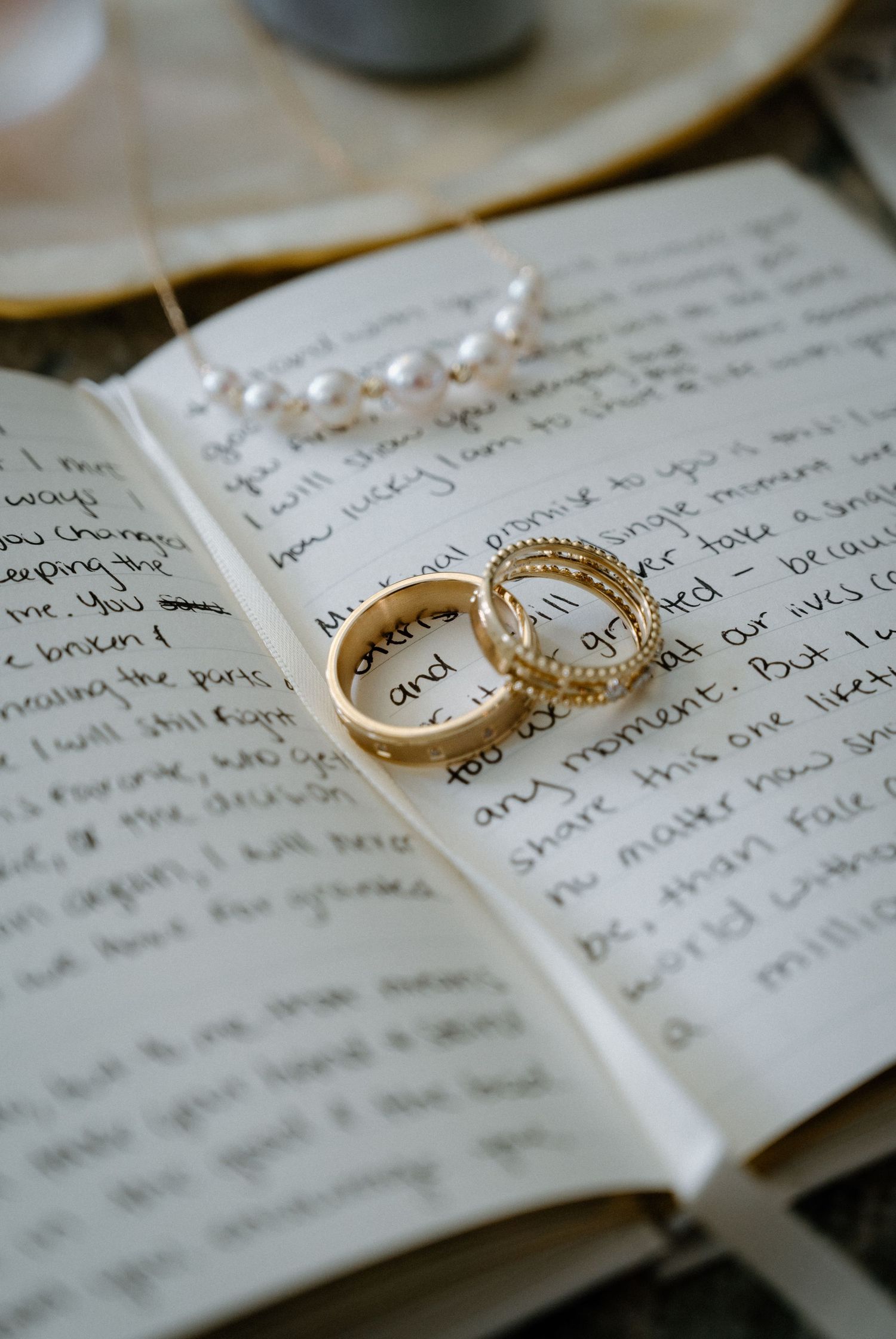 Gold wedding rings and pearl necklace resting on handwritten wedding vows in an open journal.