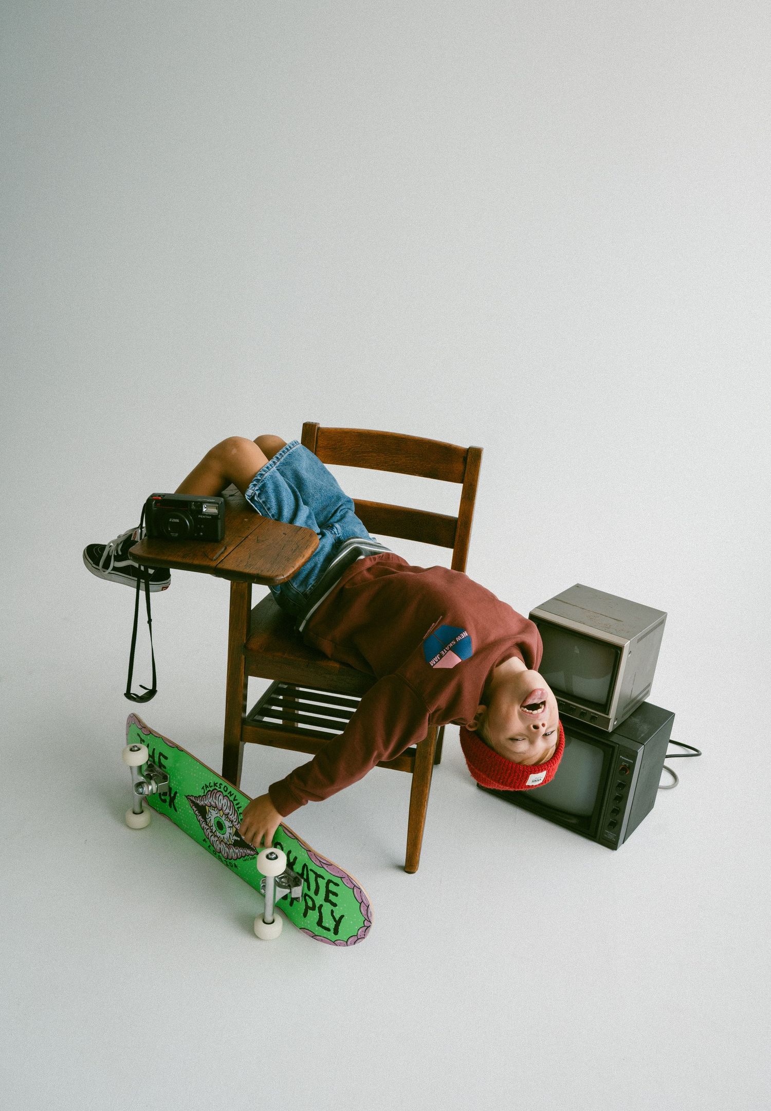 Creative studio portrait of child leaning back on chair with skateboard and vintage TV.