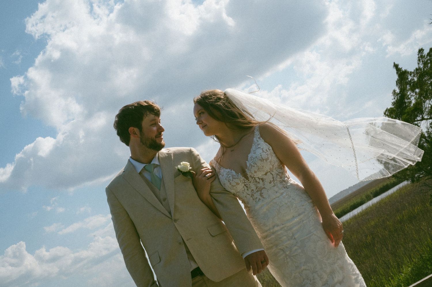 Bride and groom gazing at each other under a dramatic cloudy sky with veil blowing in the wind.