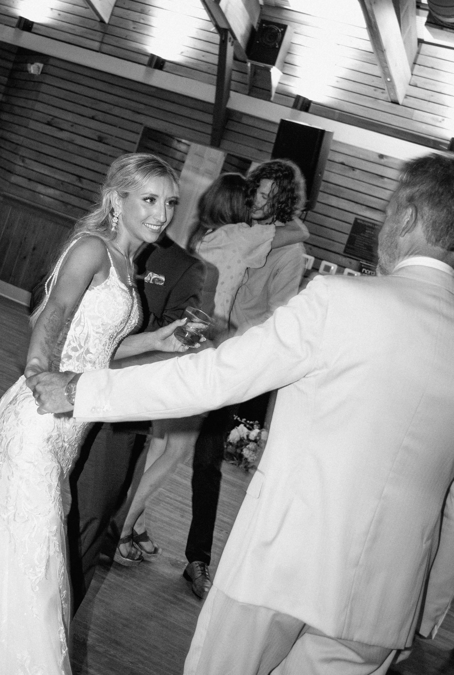 Bride smiles while dancing with a guest in black and white wedding reception photo.