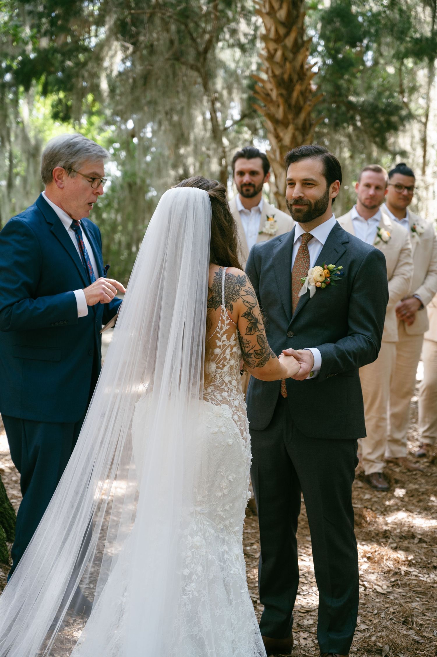 Officiant reads ceremony script as groom holds bride's hands at outdoor woodland wedding.