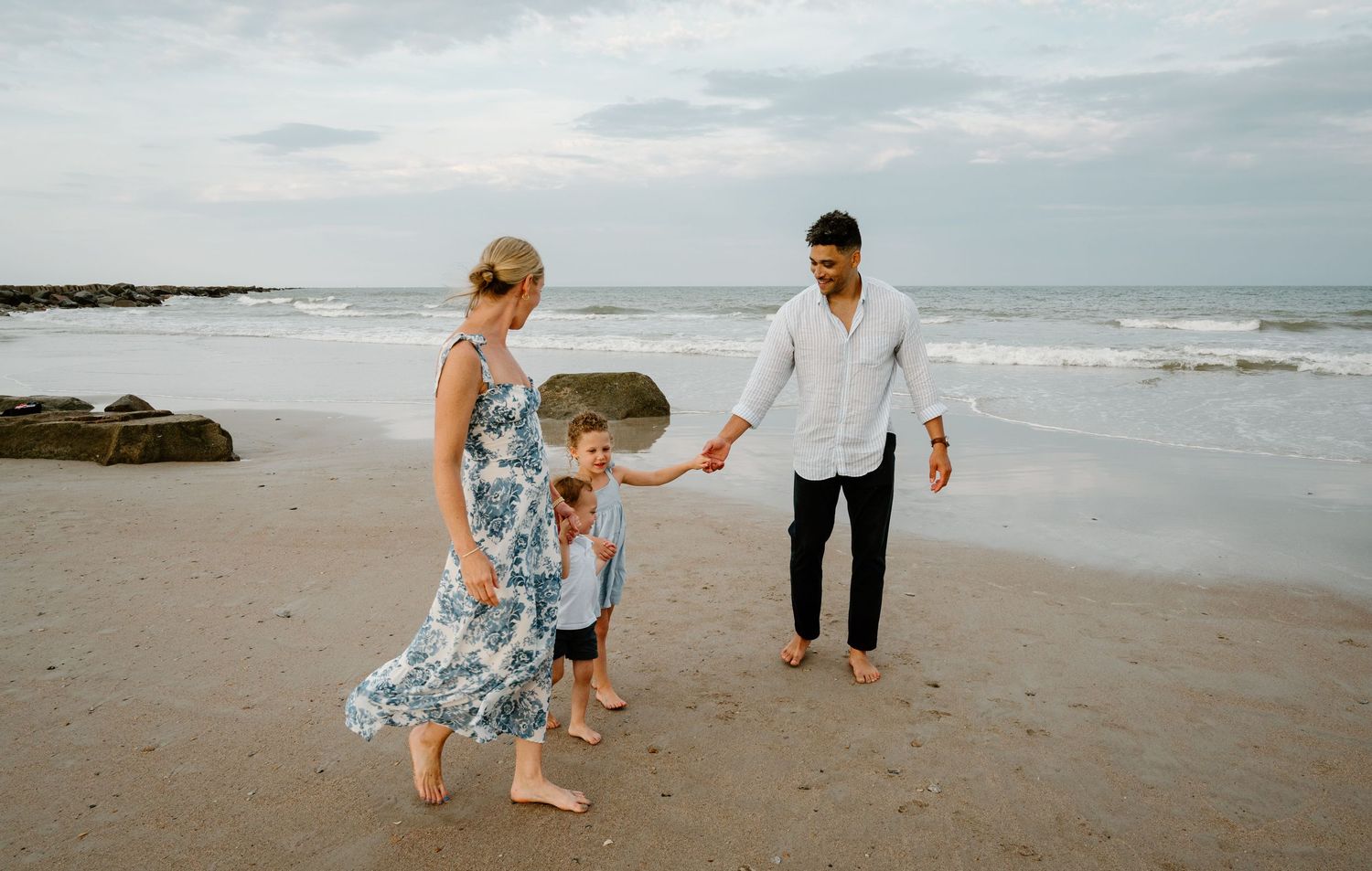 Young family of three walking hand in hand along a scenic sandy beach near the ocean on Amelia Island, Florida