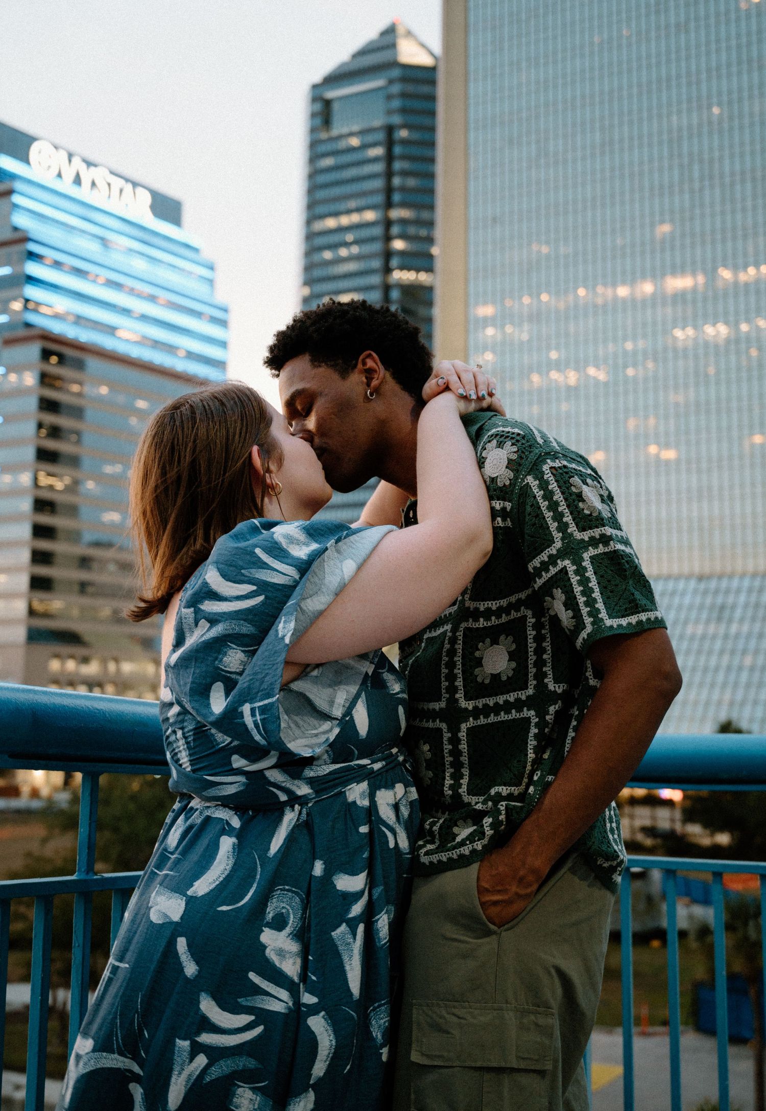 Interracial couple sharing a kiss on a bridge with city skyscrapers in the background in Jacksonville, Florida.