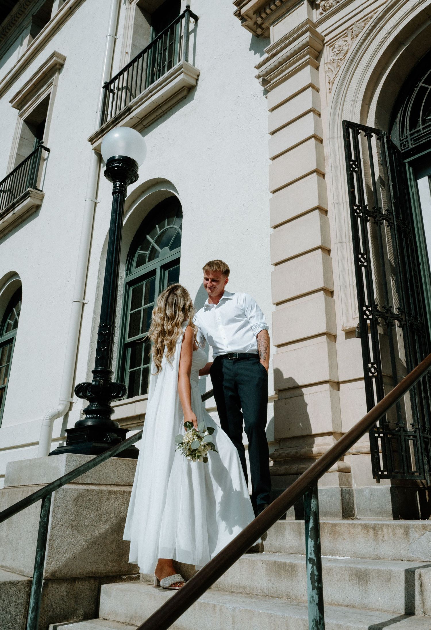Bride and groom sharing a glance on steps of elegant white neoclassical courthouse building.