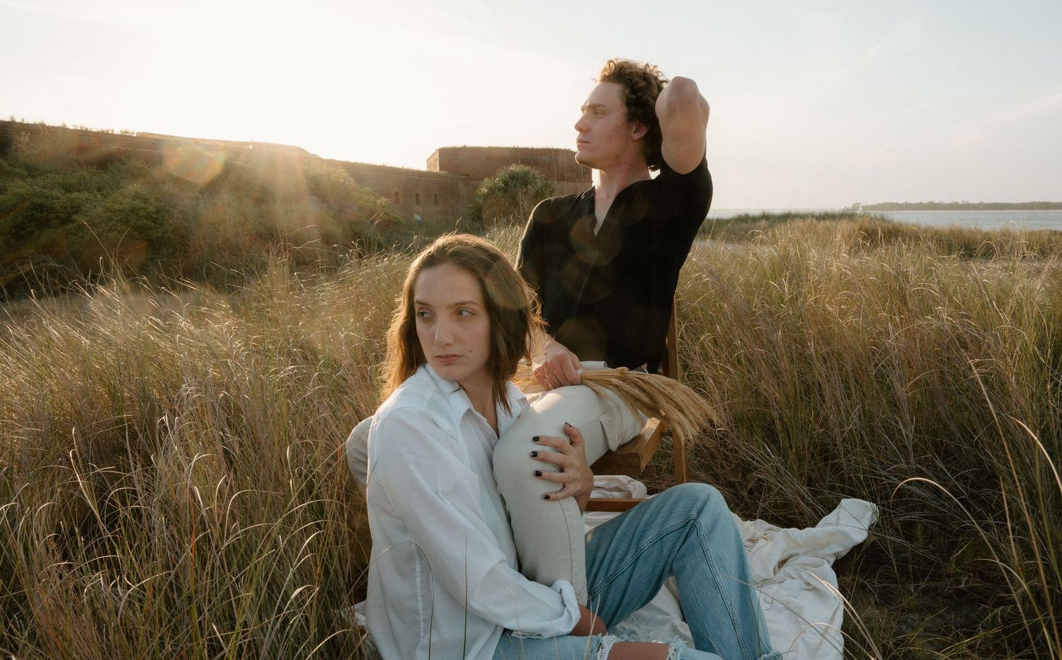 Two women sitting together in a golden sunlit field near the coast at sunset on Amelia Island, Florida