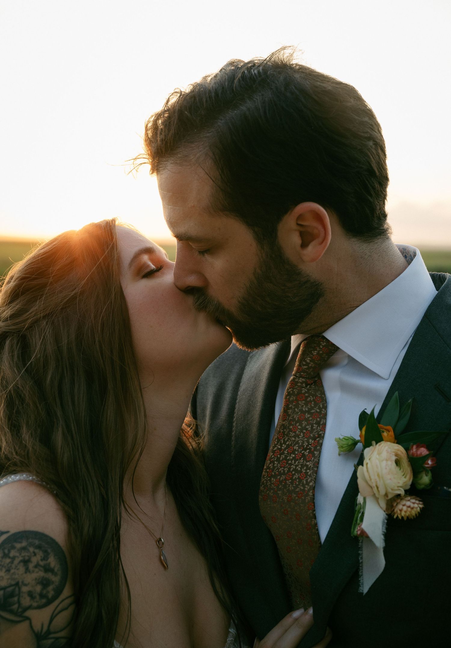 Bride and groom sharing a golden hour kiss with warm sunset light glowing behind them.