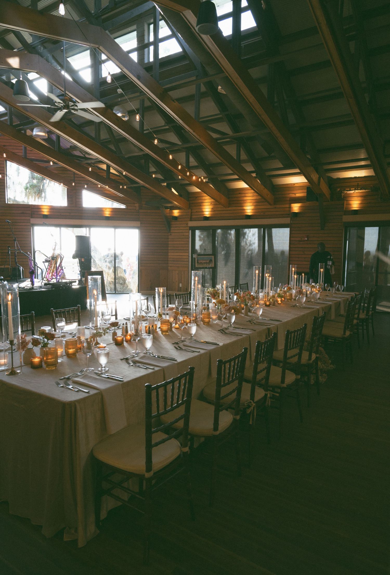 Elegant rustic wedding reception hall with long tables, candles, and wood beam ceiling.