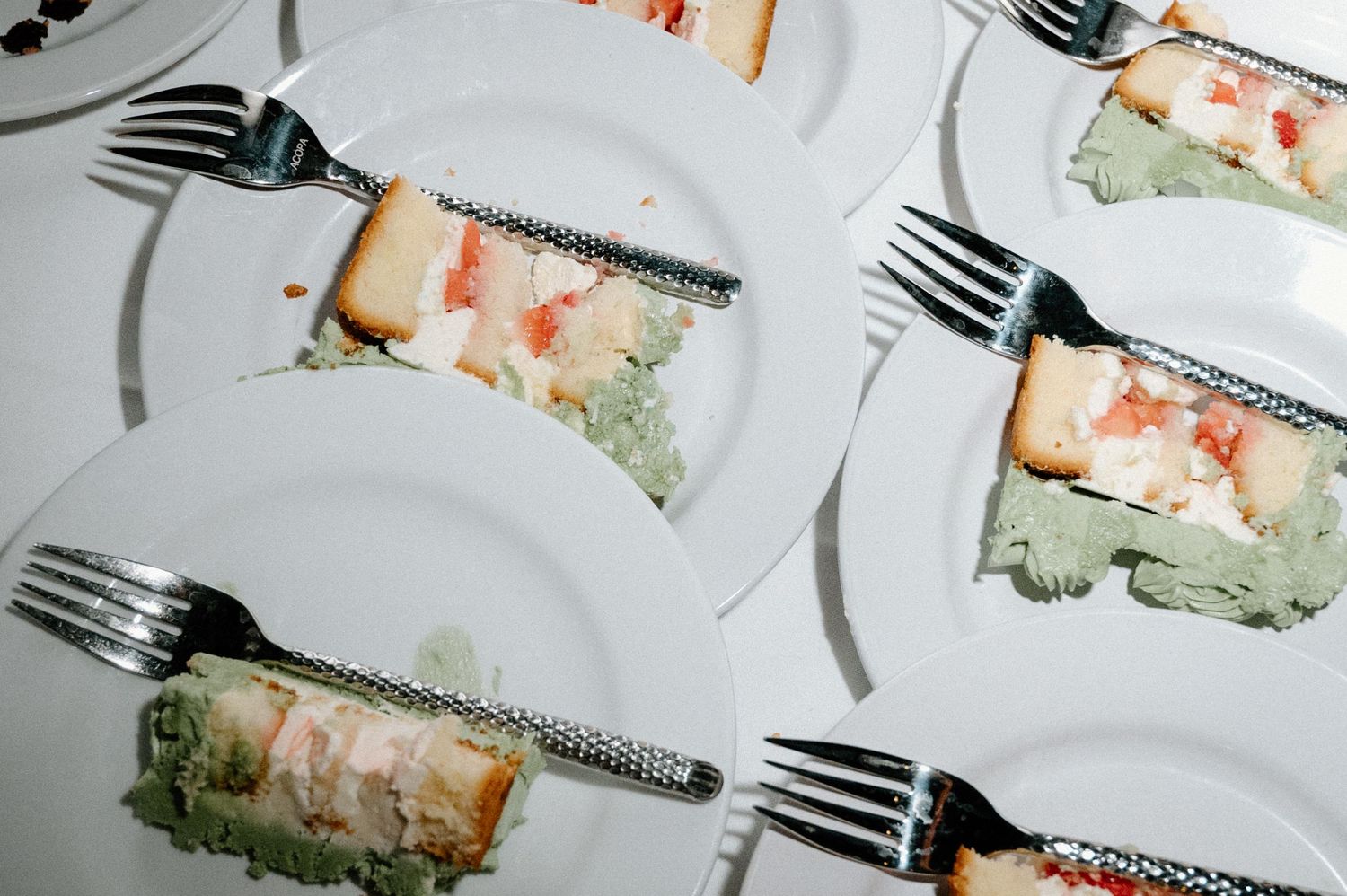 Overhead view of plated wedding cake slices with forks on white plates at reception.