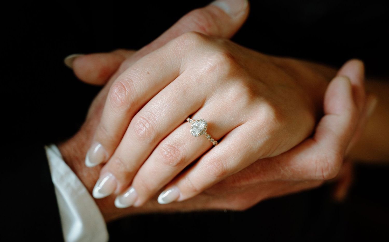 Close-up of an elegant diamond engagement ring on a womans hand resting on partners hand.