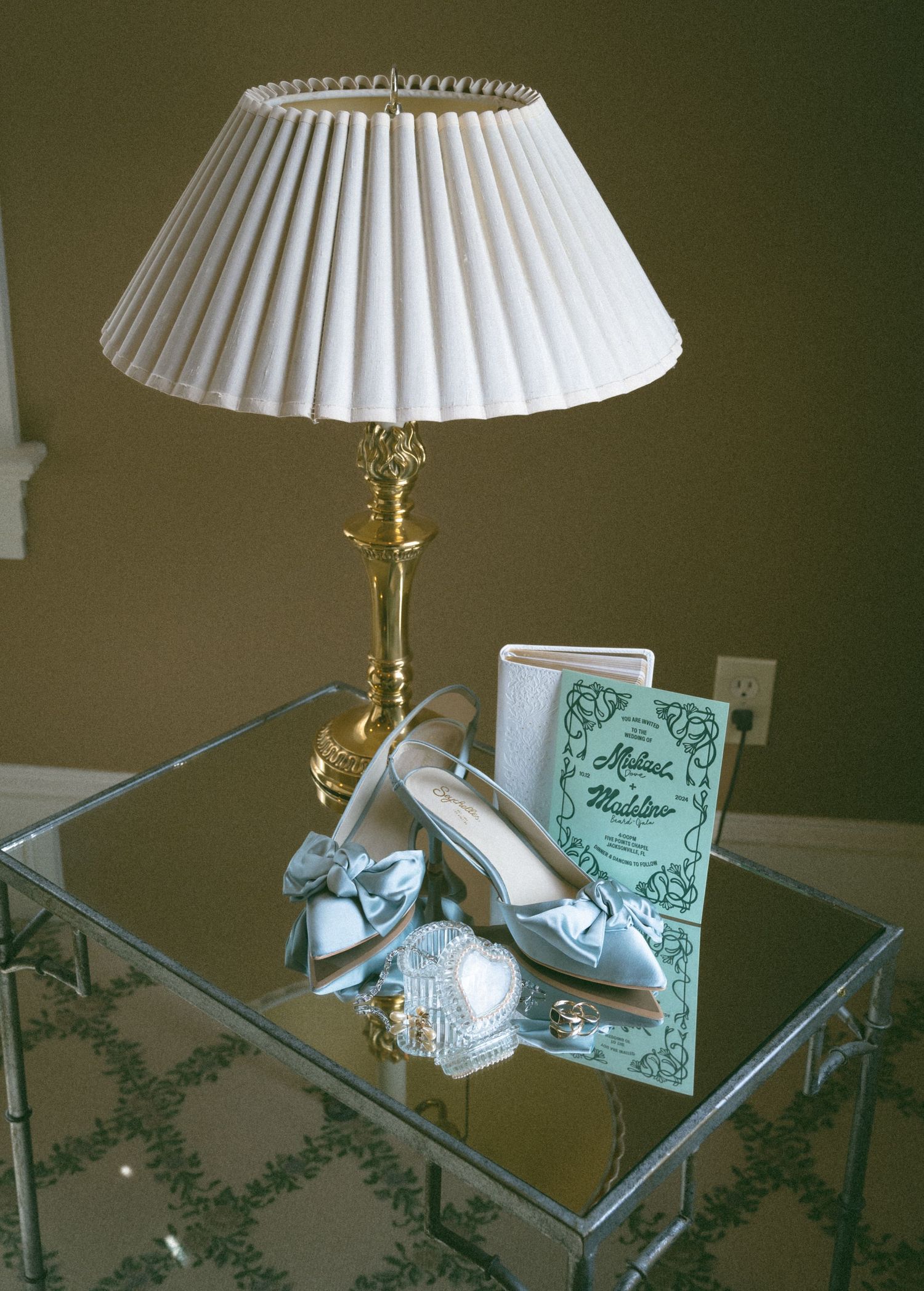 Elegant silver bridal heels displayed beside a framed card and crystal heart on a mirrored glass table.
