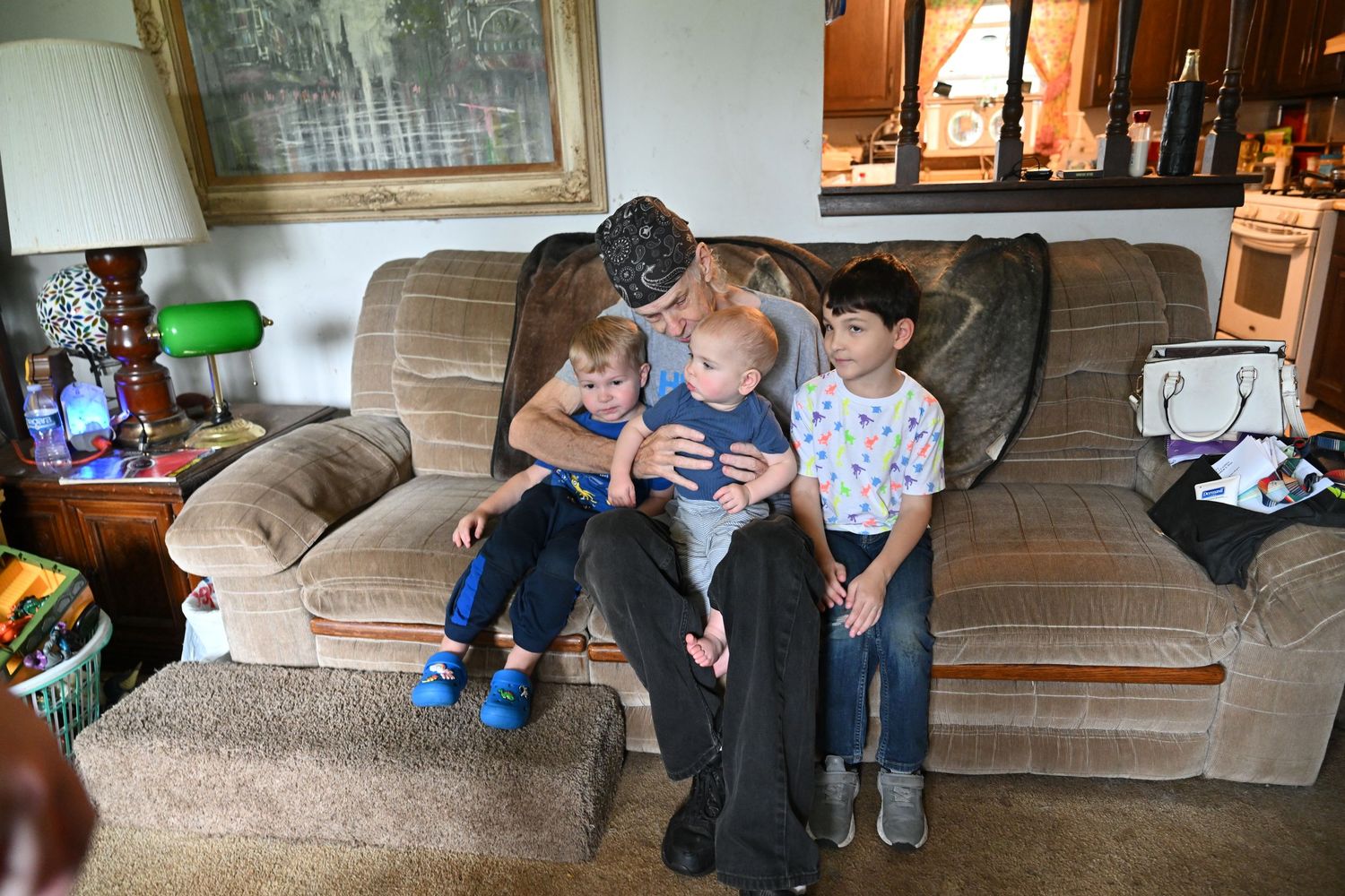 Older gentleman sits on couch with three young children looking at a smartphone in a cozy living room.