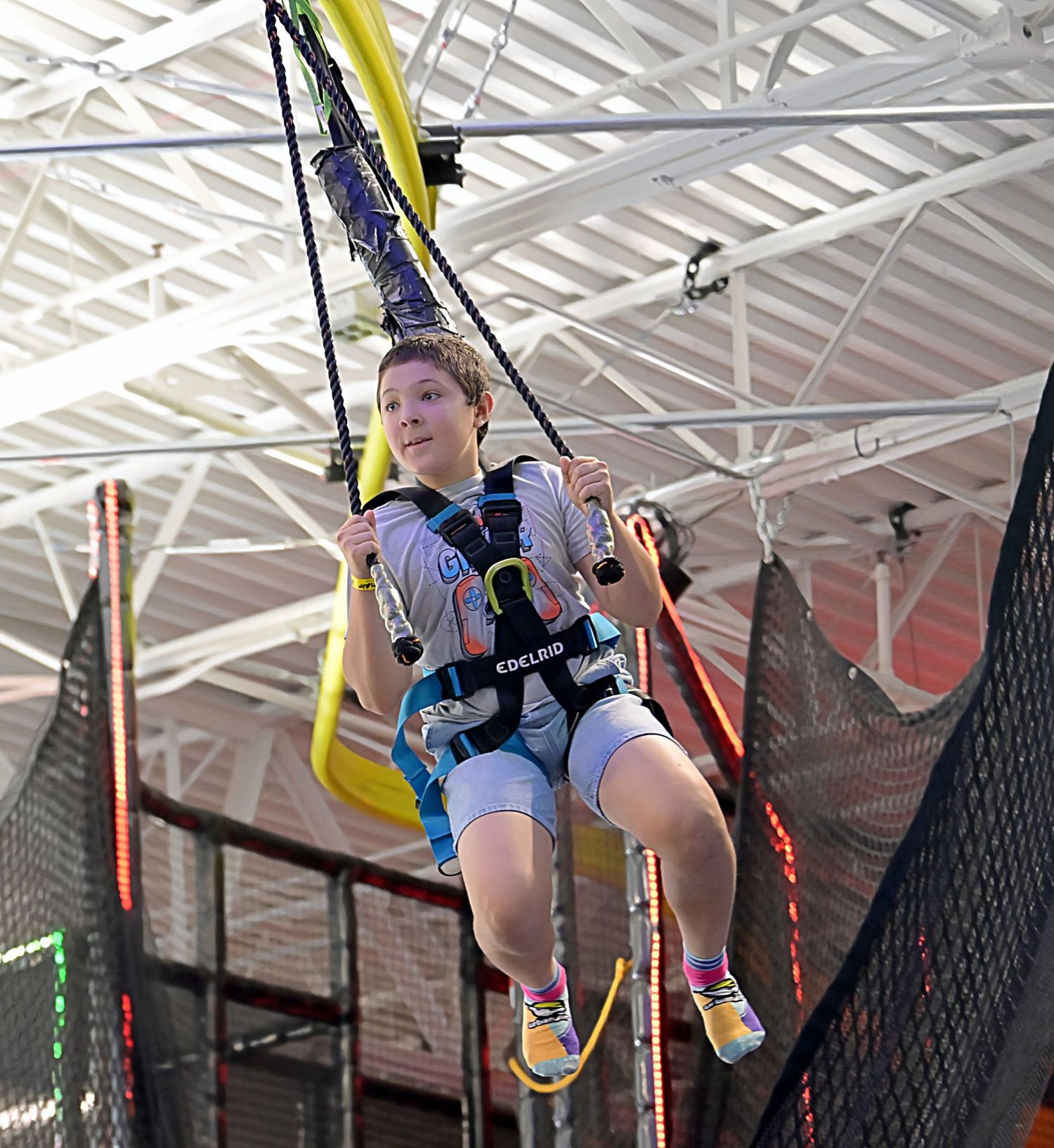 A child in a harness soars on a zip line attraction inside a colorful indoor adventure park.