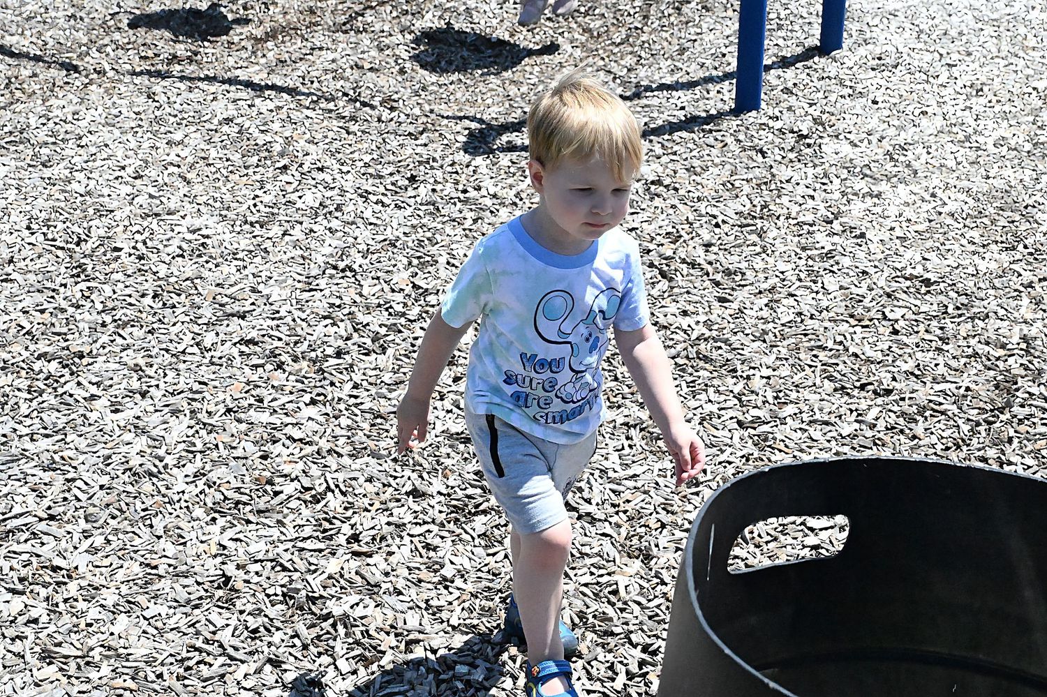 Young toddler boy walking on a gravel playground on a sunny day.