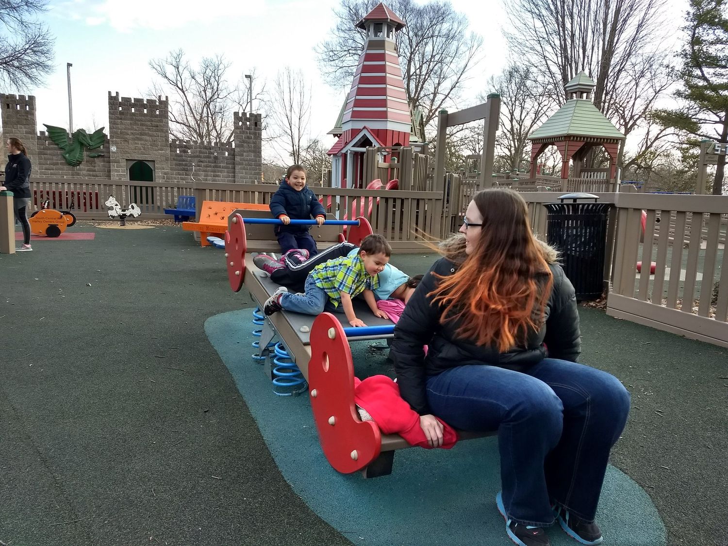 A woman and children enjoying a castle-themed playground on a cloudy day.
