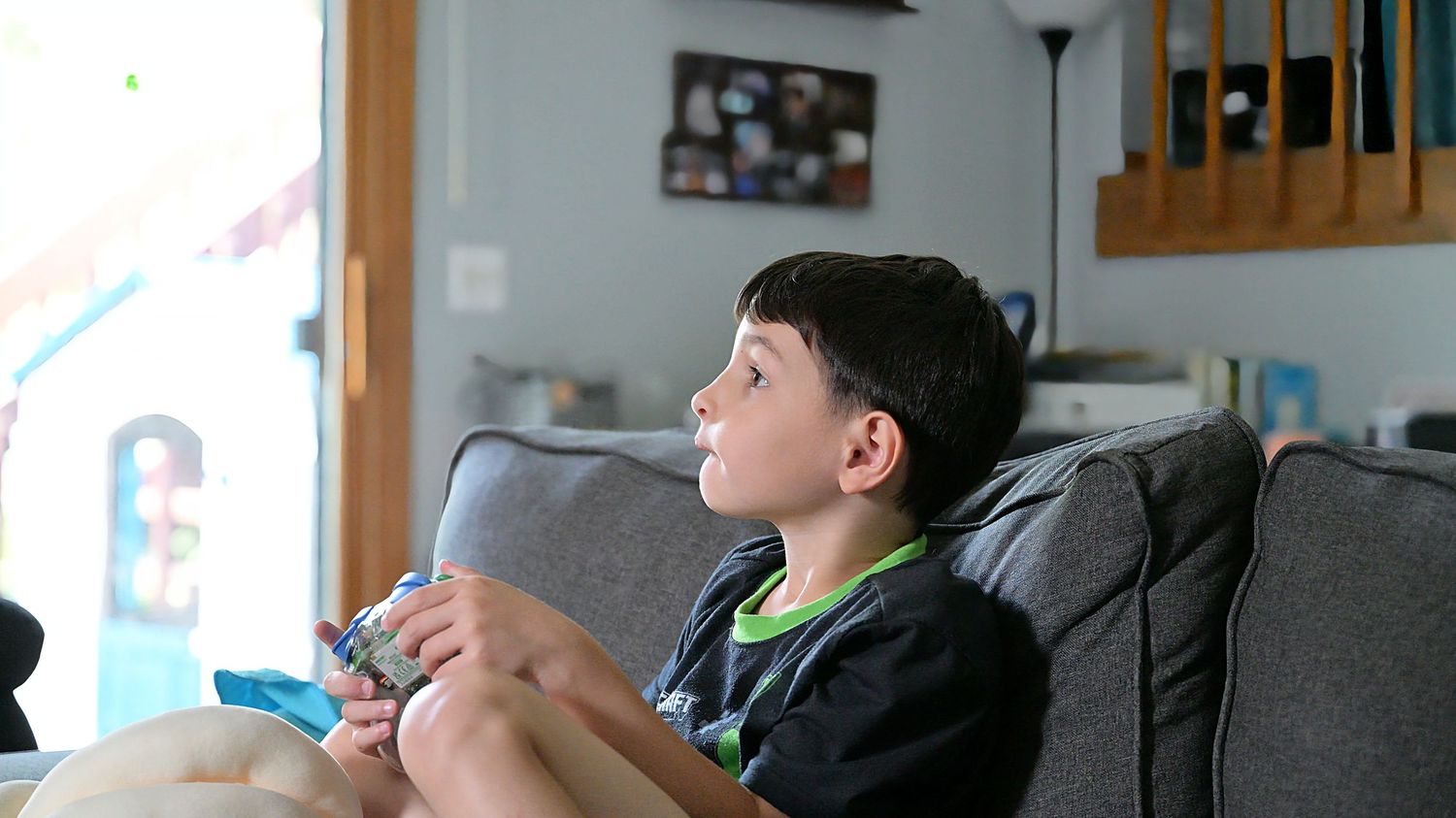 Young boy focused on handheld video game on couch.