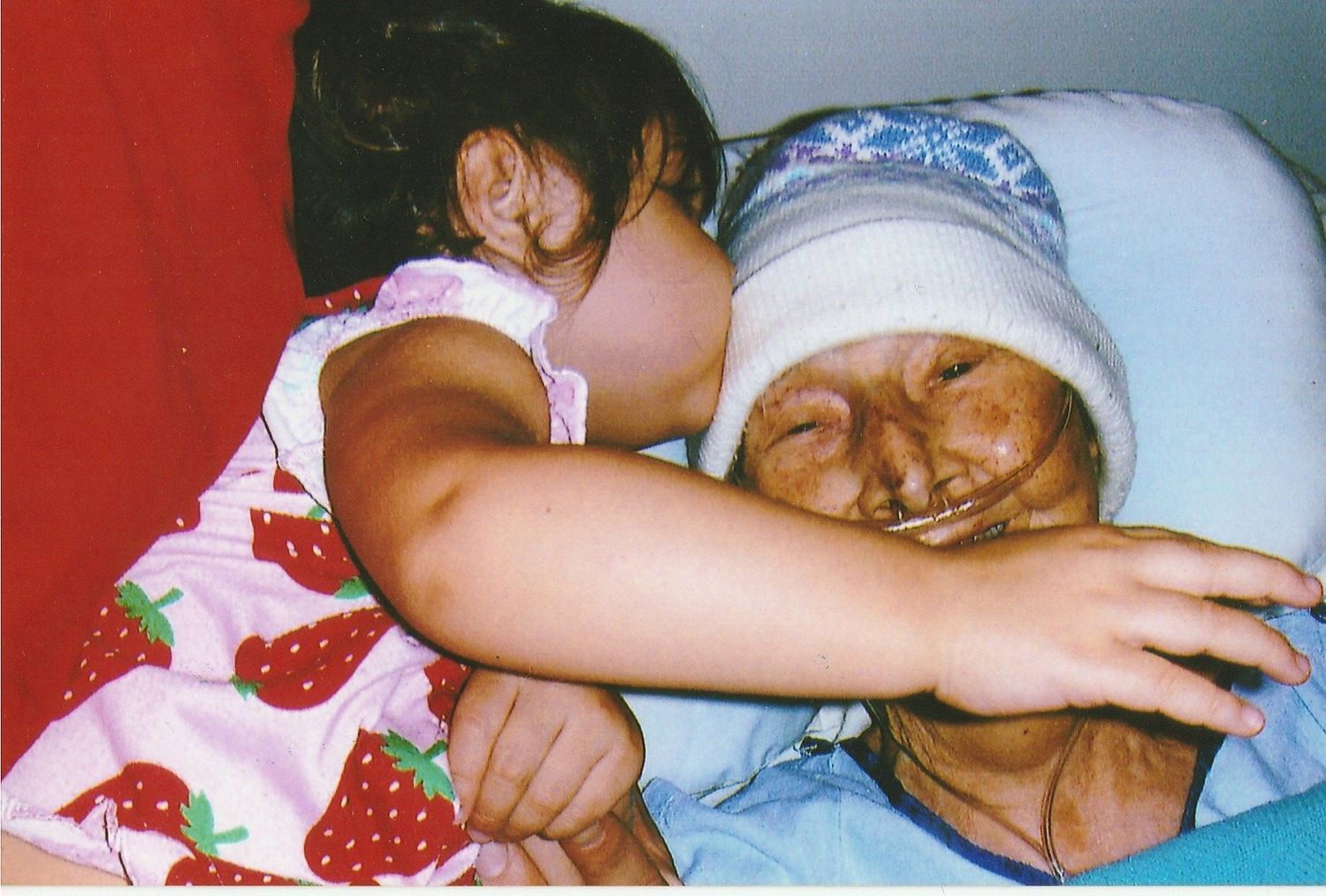 Young girl hugging and embracing an elderly person lying in bed.