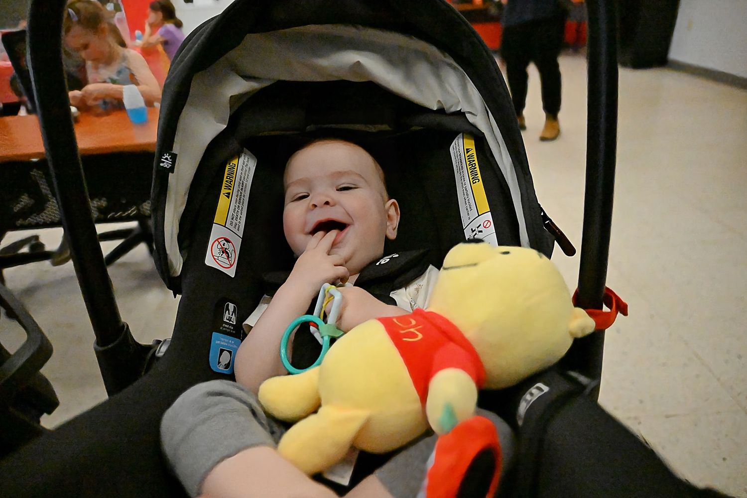 Smiling baby relaxing in a car seat with a Winnie the Pooh stuffed toy.