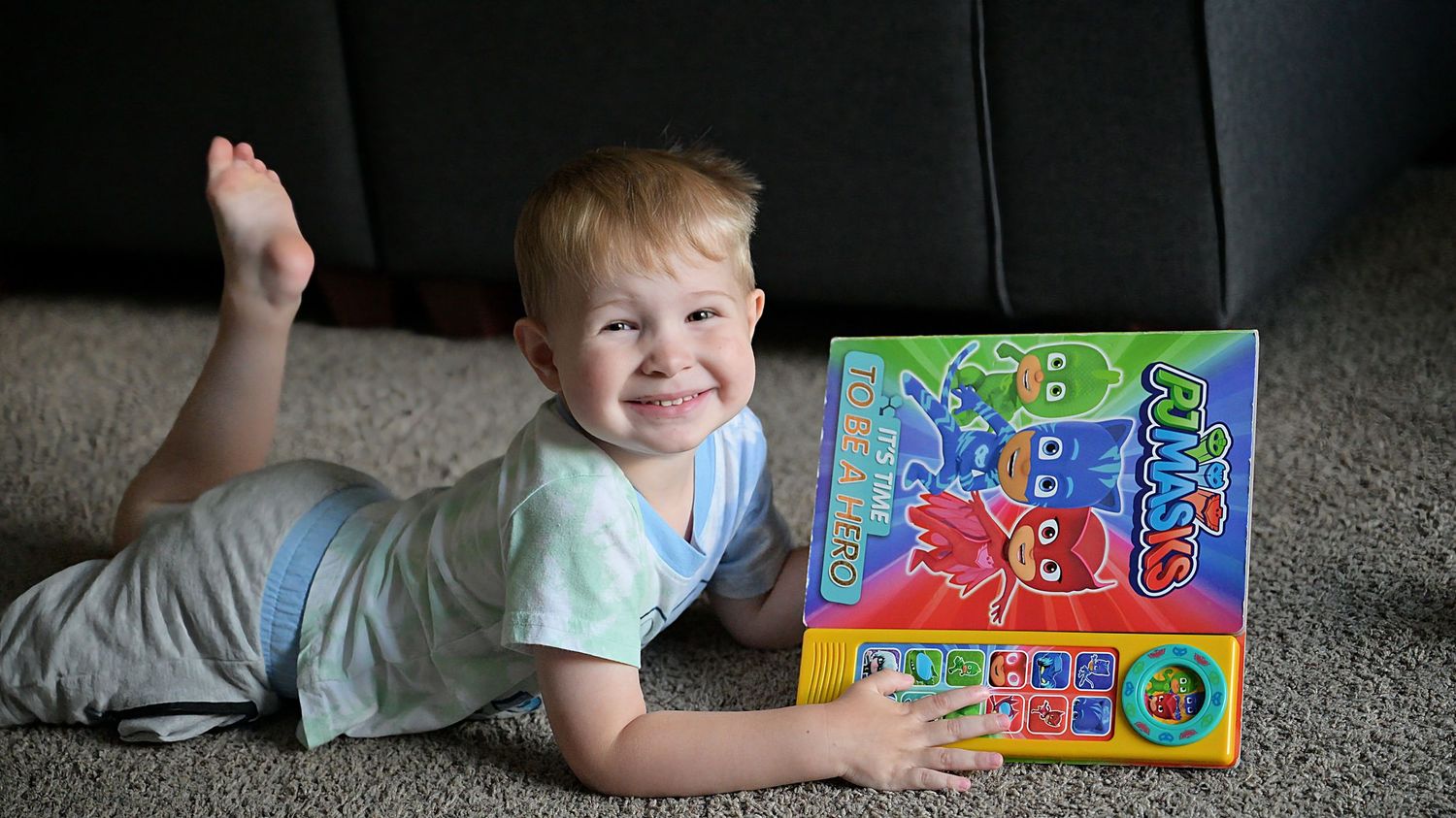 Happy toddler lying on floor with colorful PJ Masks book.