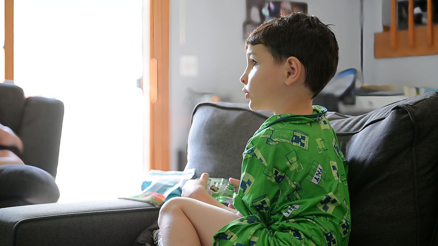 Child in green Minecraft outfit relaxing on dark sofa.