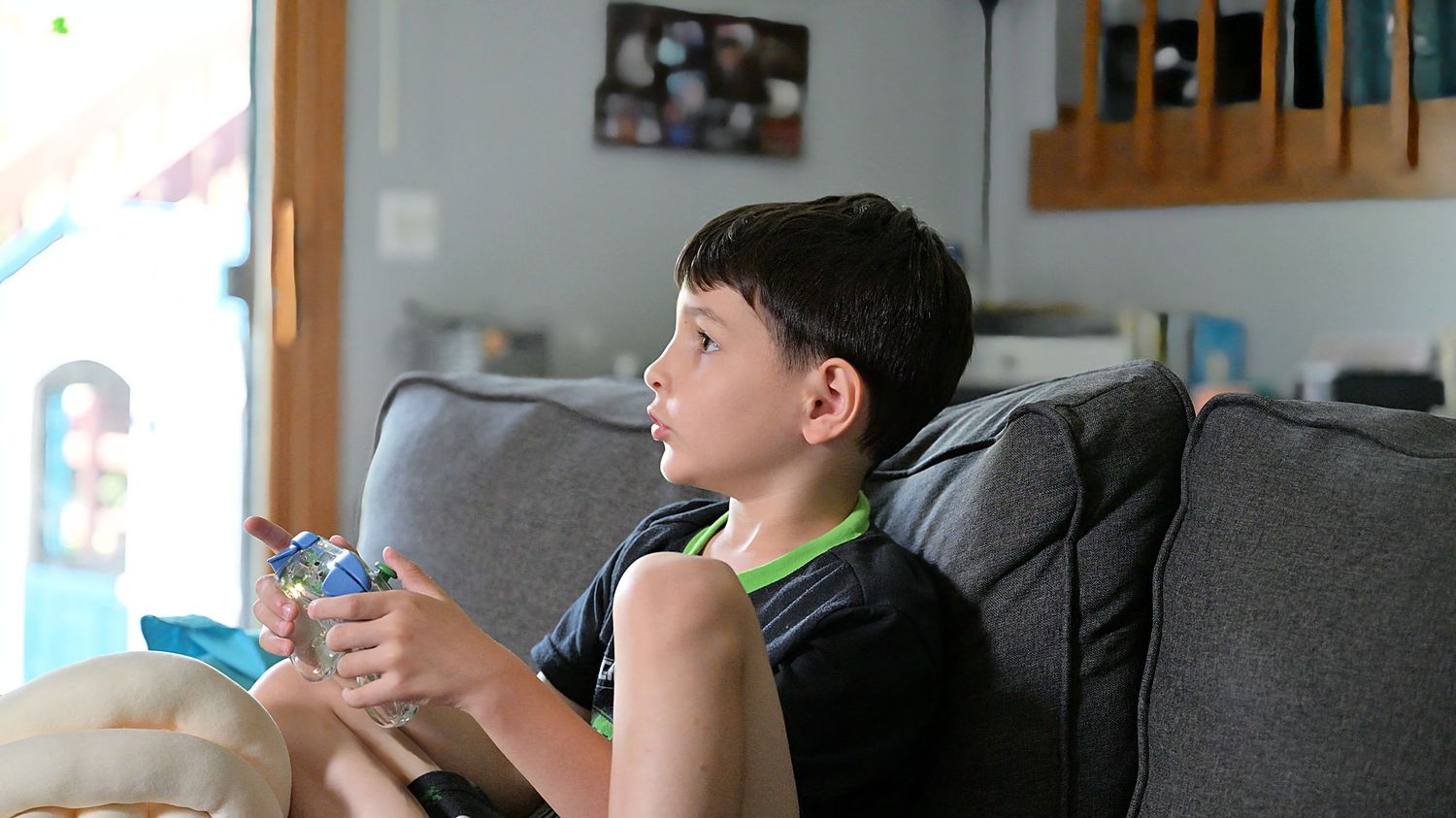 Boy playing video games on gray sofa at home.