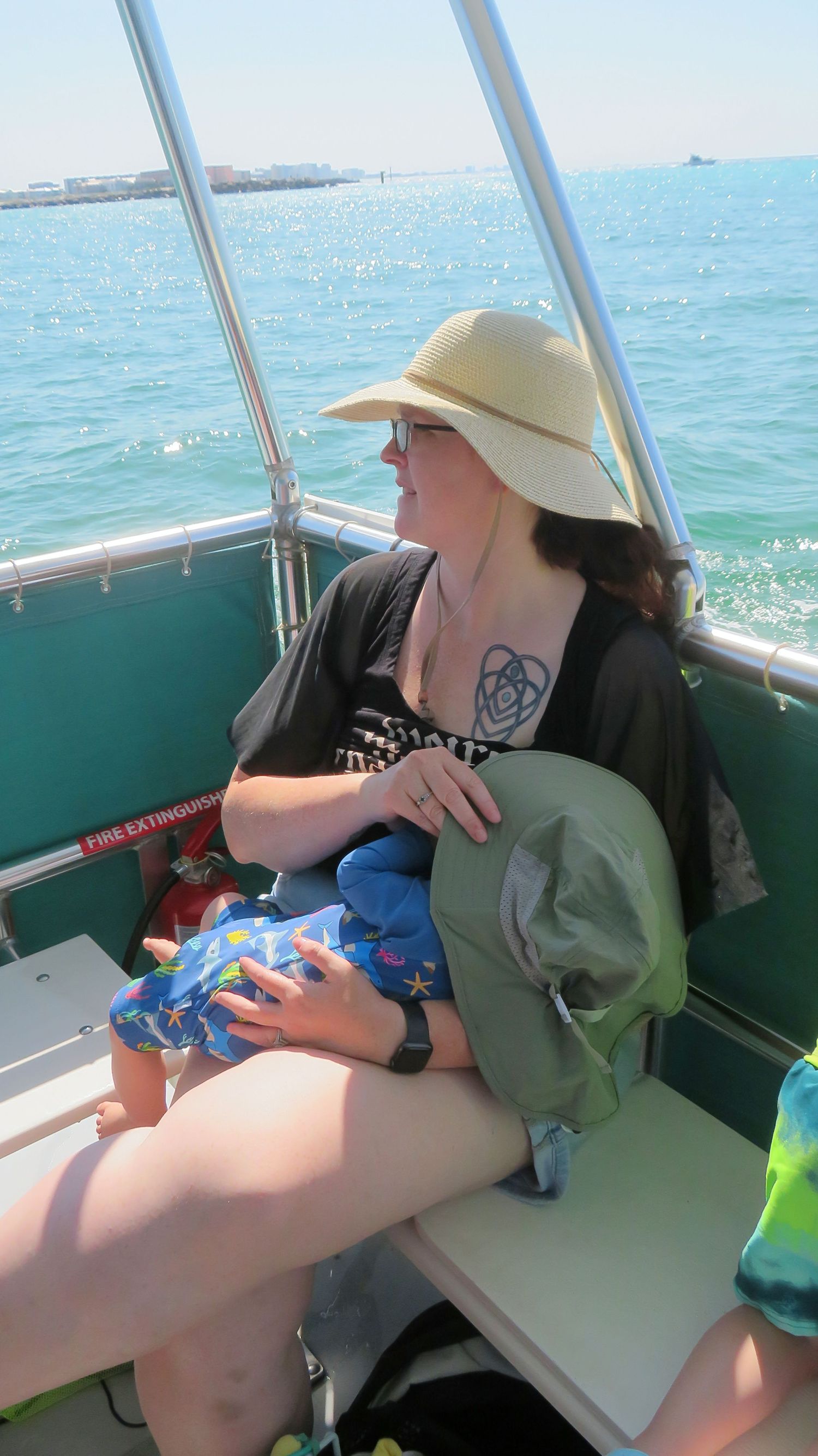 Woman in wide-brim sun hat sitting on a boat holding a baby on a bright sunny day.