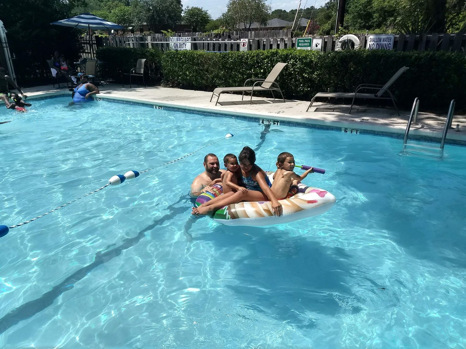A group of people floating on an inflatable ring in a sunny outdoor pool.