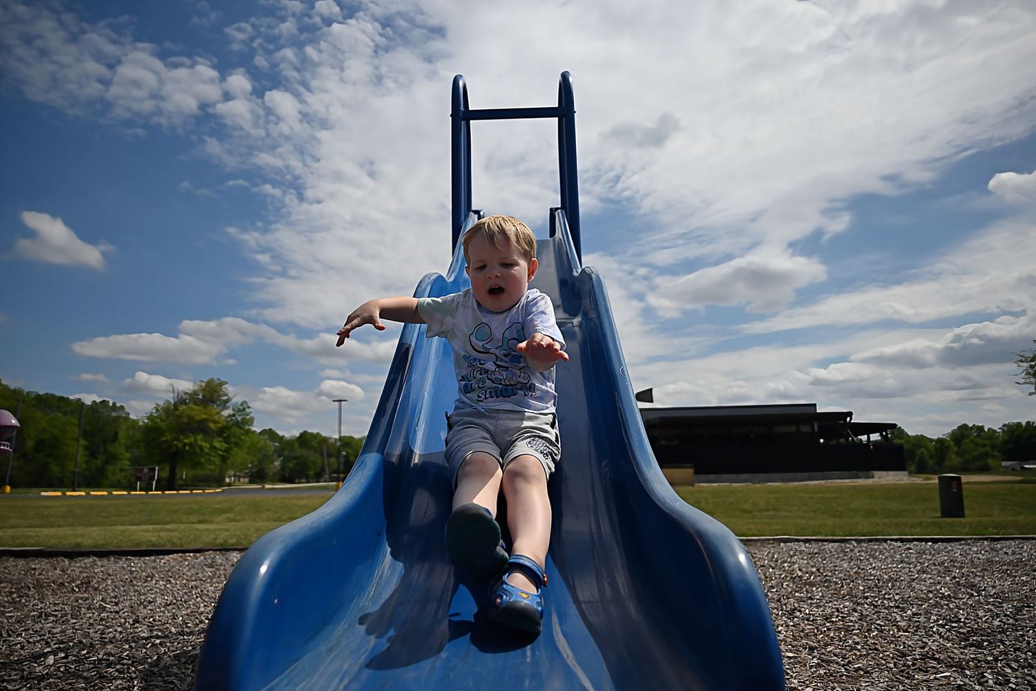 Happy toddler sliding down a blue playground slide on a sunny day.