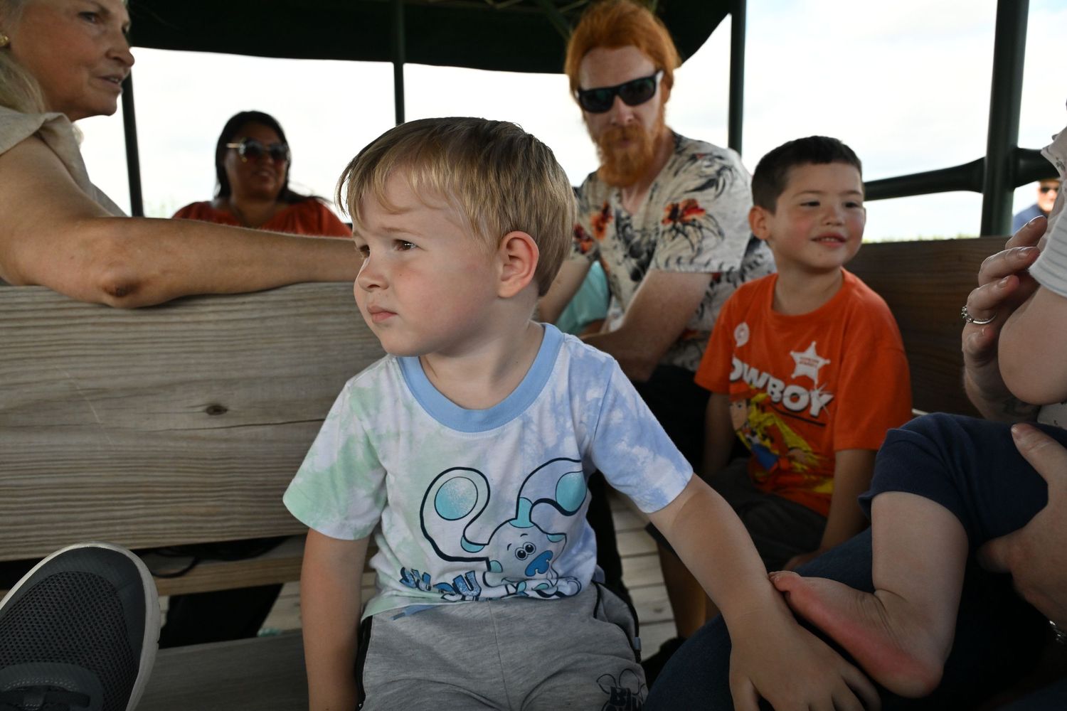 Two young boys sit on a wagon ride while adults sit behind them on a sunny day.