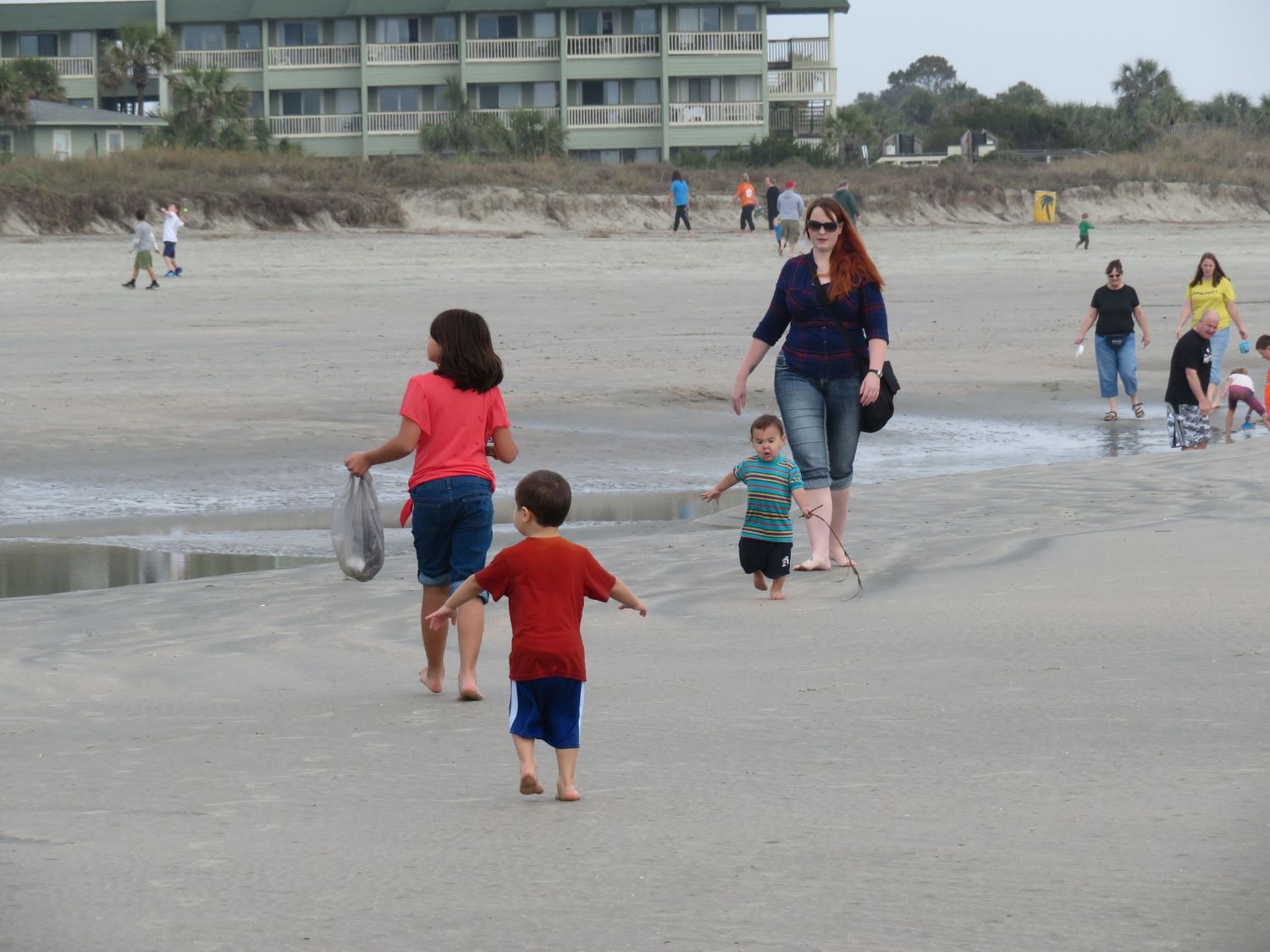 A woman and children playing on a sandy beach near the ocean waves.