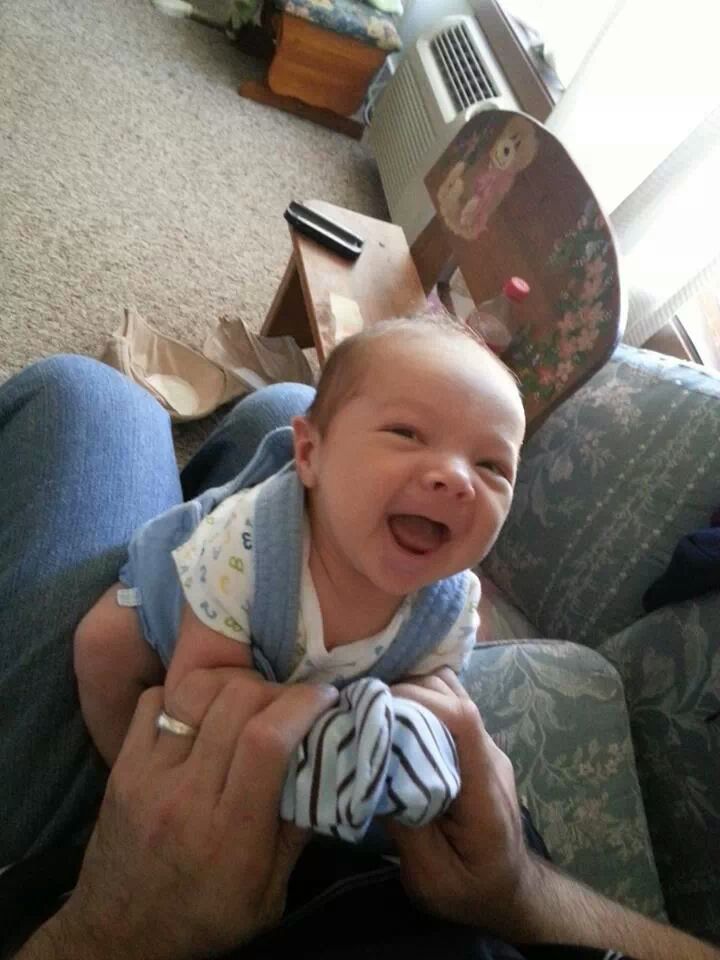 A laughing newborn baby being held by an adult in a cozy living room setting.