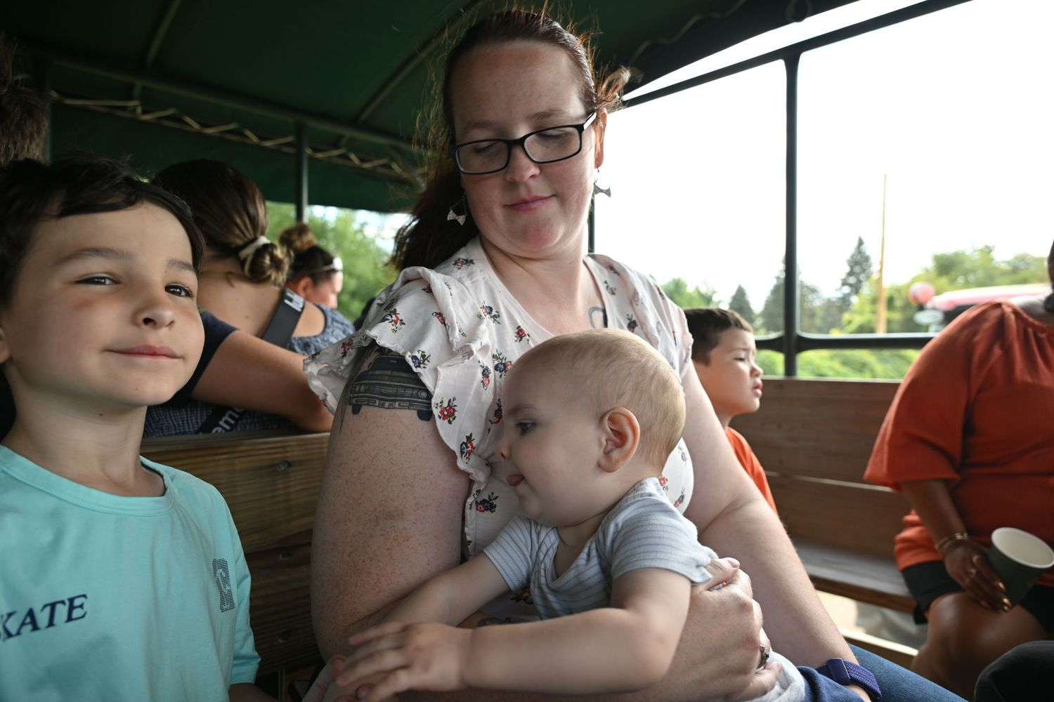 A mother holds her baby while sitting with a young boy on a hay ride.