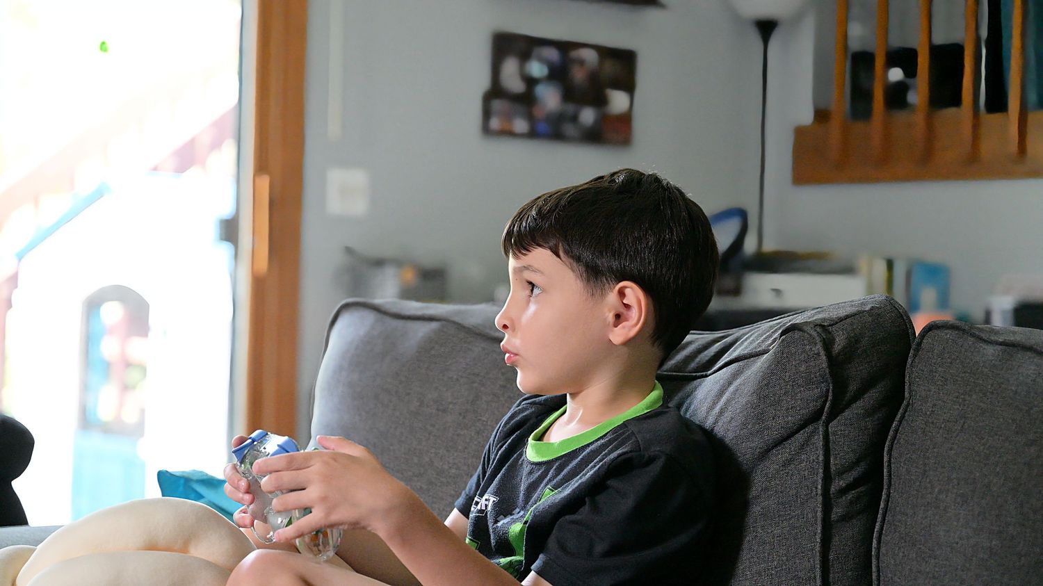 Child playing handheld game console on living room sofa.