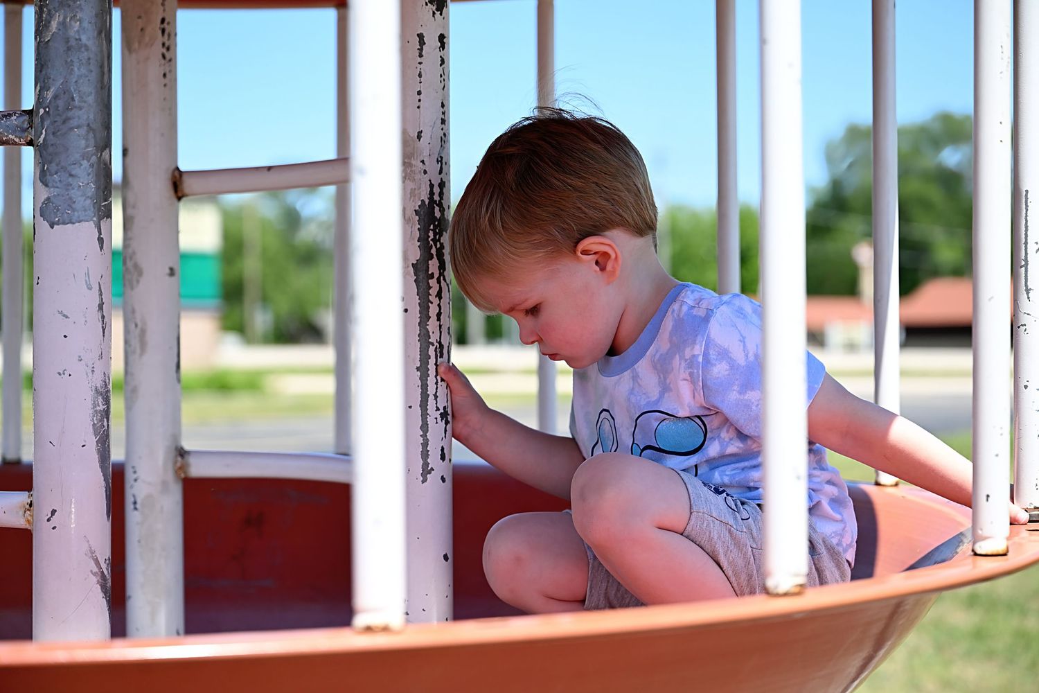 Young boy sitting inside a merry-go-round playground equipment on a sunny day.