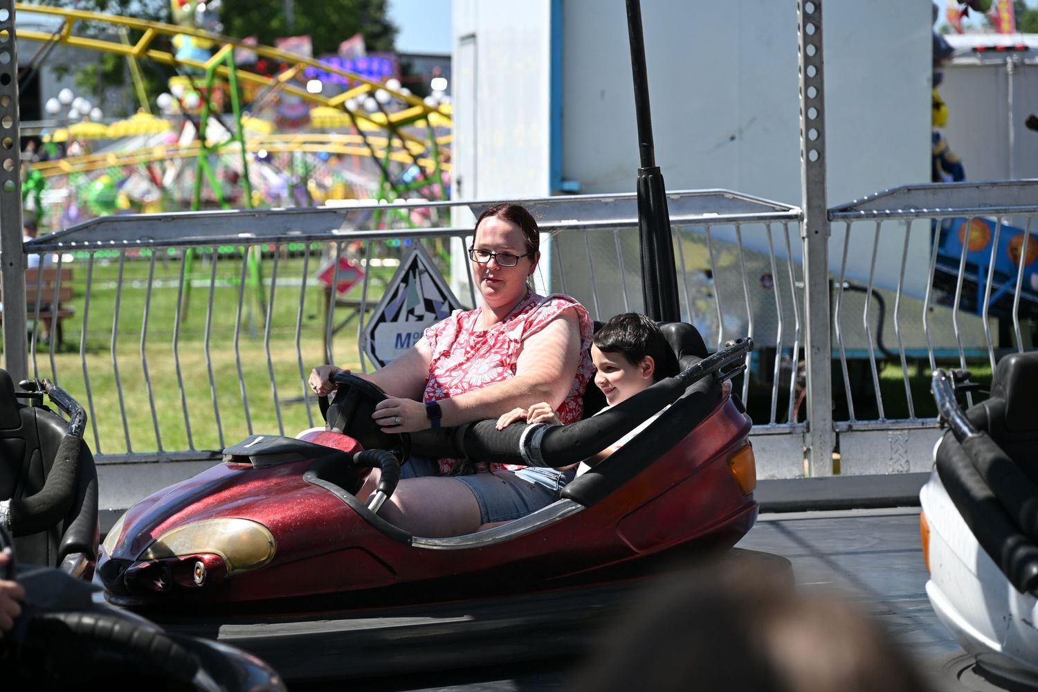Woman and child riding together in a bumper car at an outdoor carnival.