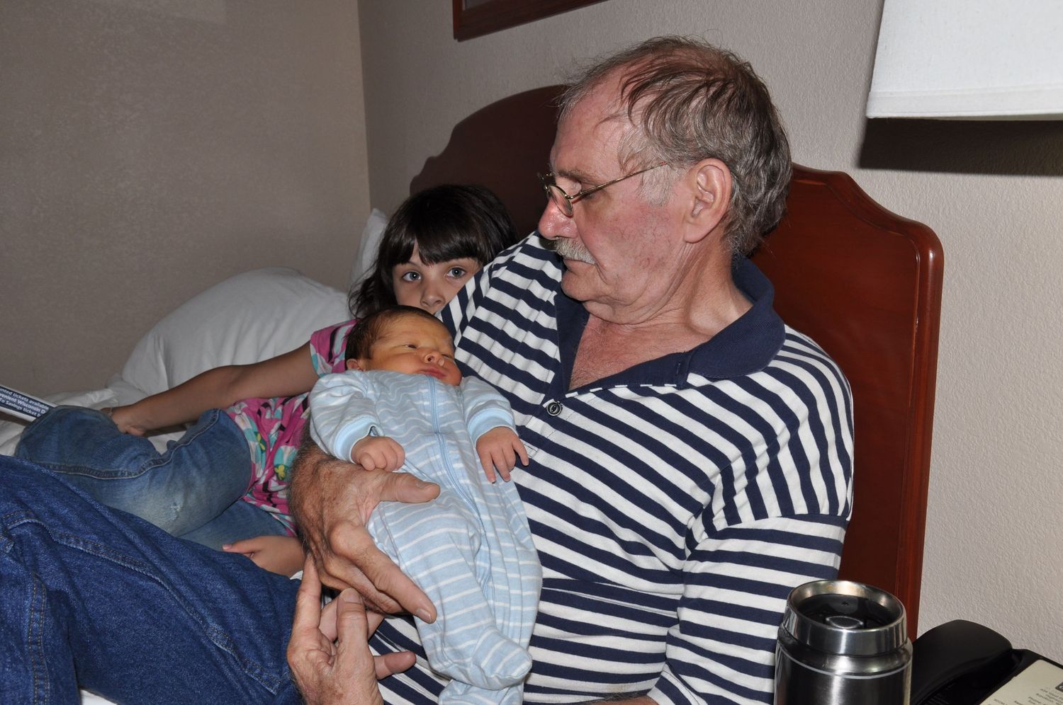 Grandfather holding newborn baby while seated in a chair indoors.