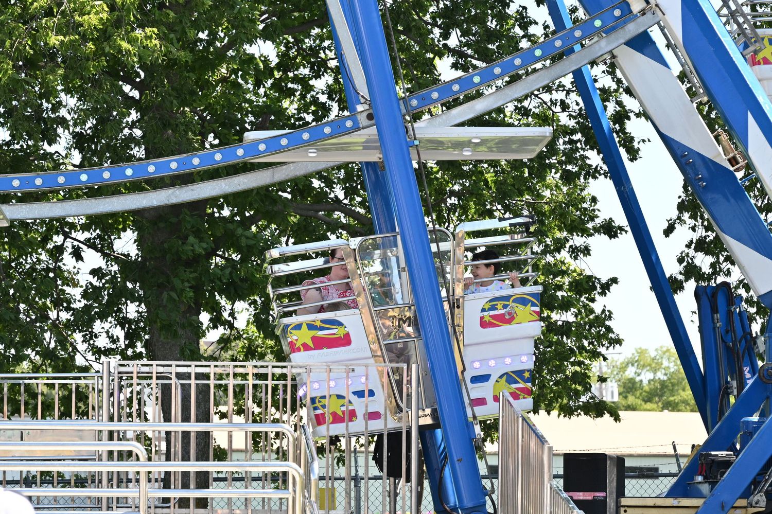 Blue and white carnival Ferris wheel ride surrounded by green trees at a fair.