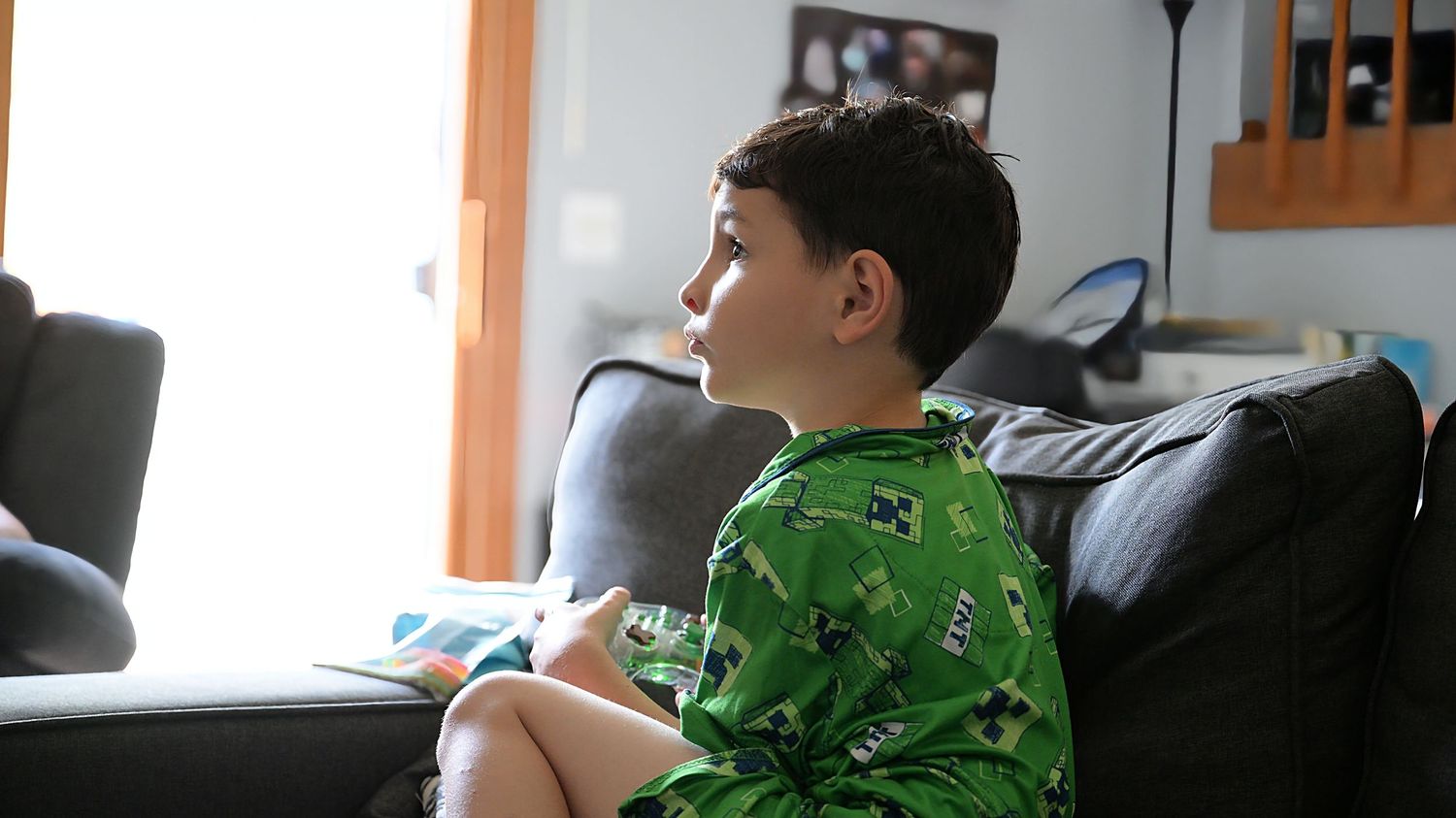 Boy in Minecraft pajamas sitting on black couch.
